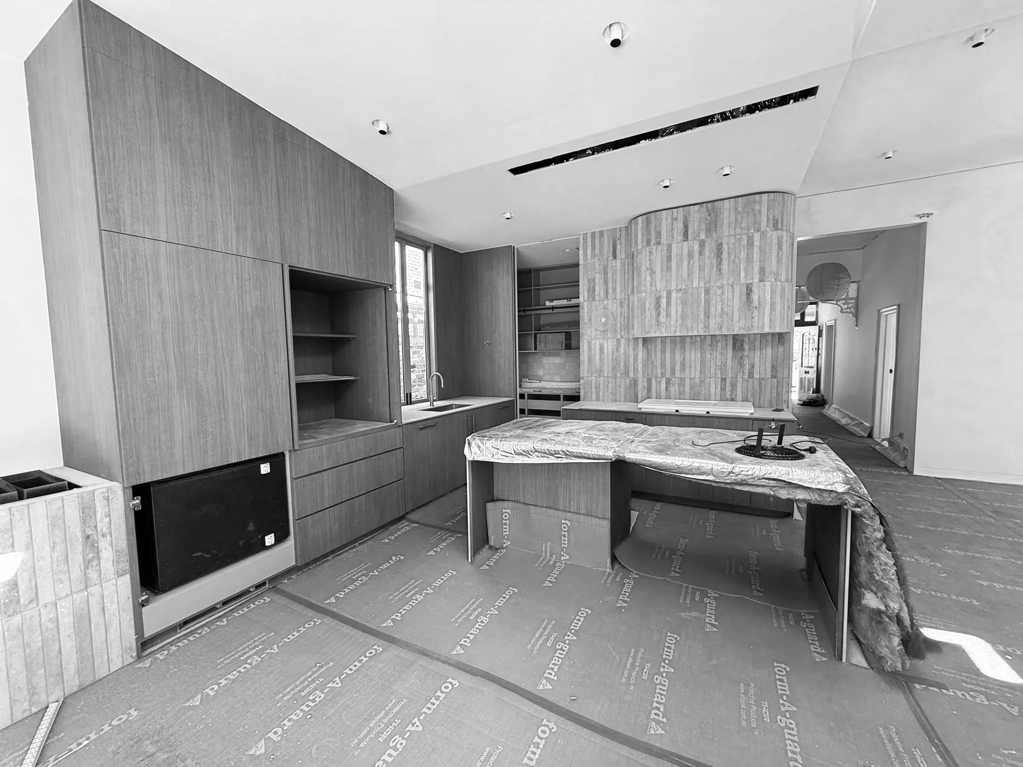Under-construction kitchen with wooden cabinets, an island with protective covering, and construction materials on the floor.