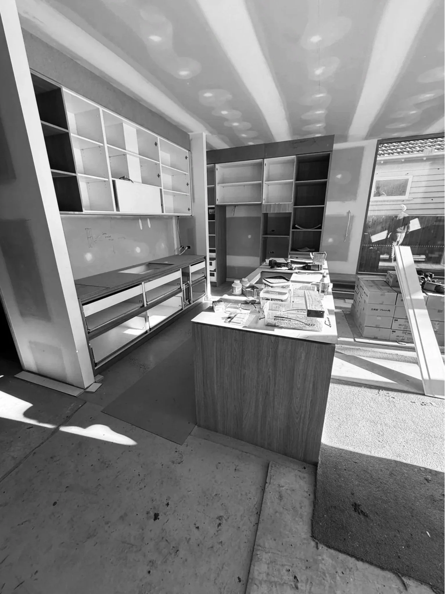 Kitchen under renovation with unfinished cabinets, cluttered work table, and construction materials.