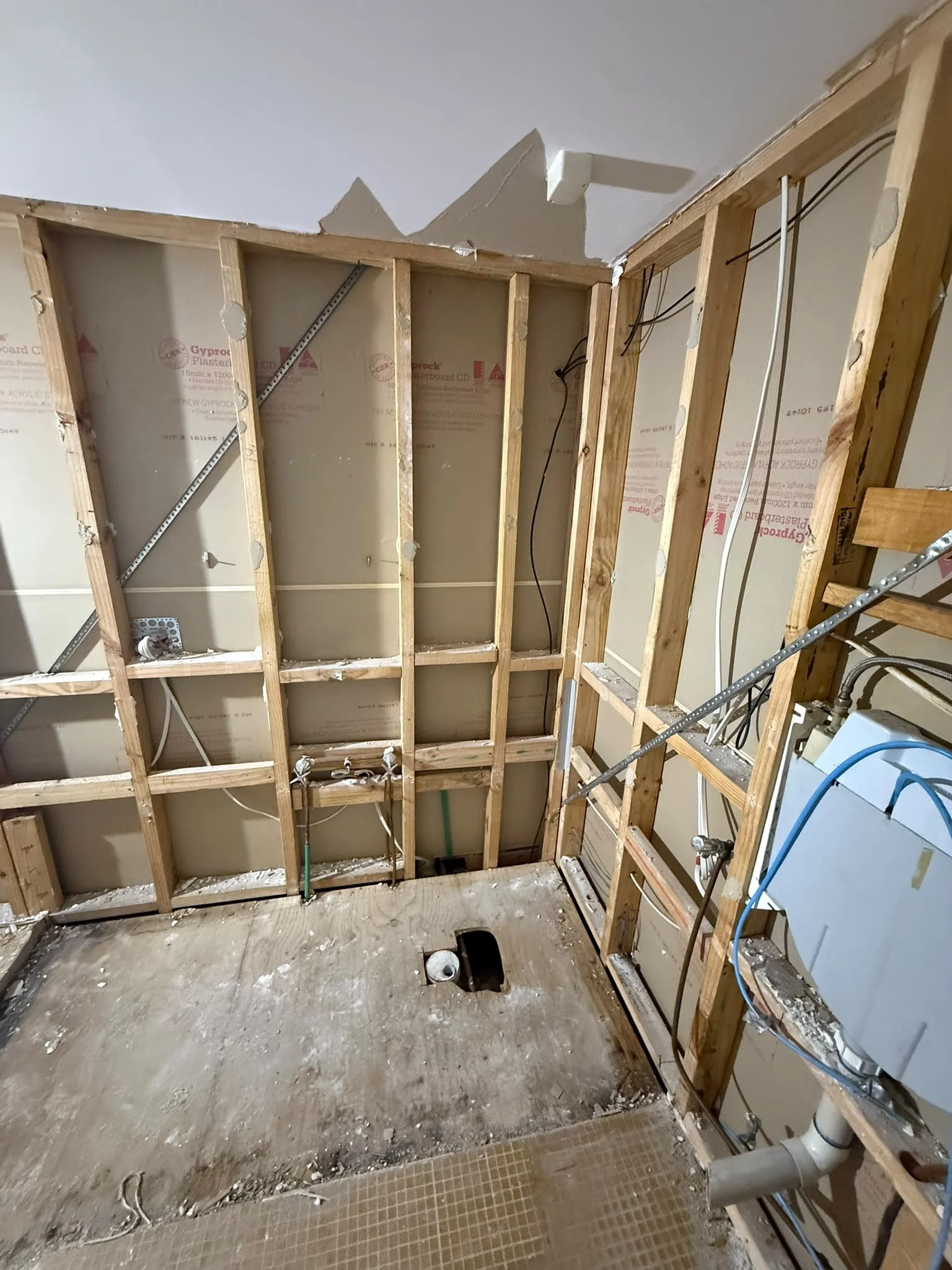 Construction site with exposed wooden framing and plumbing pipes in an incomplete room.
