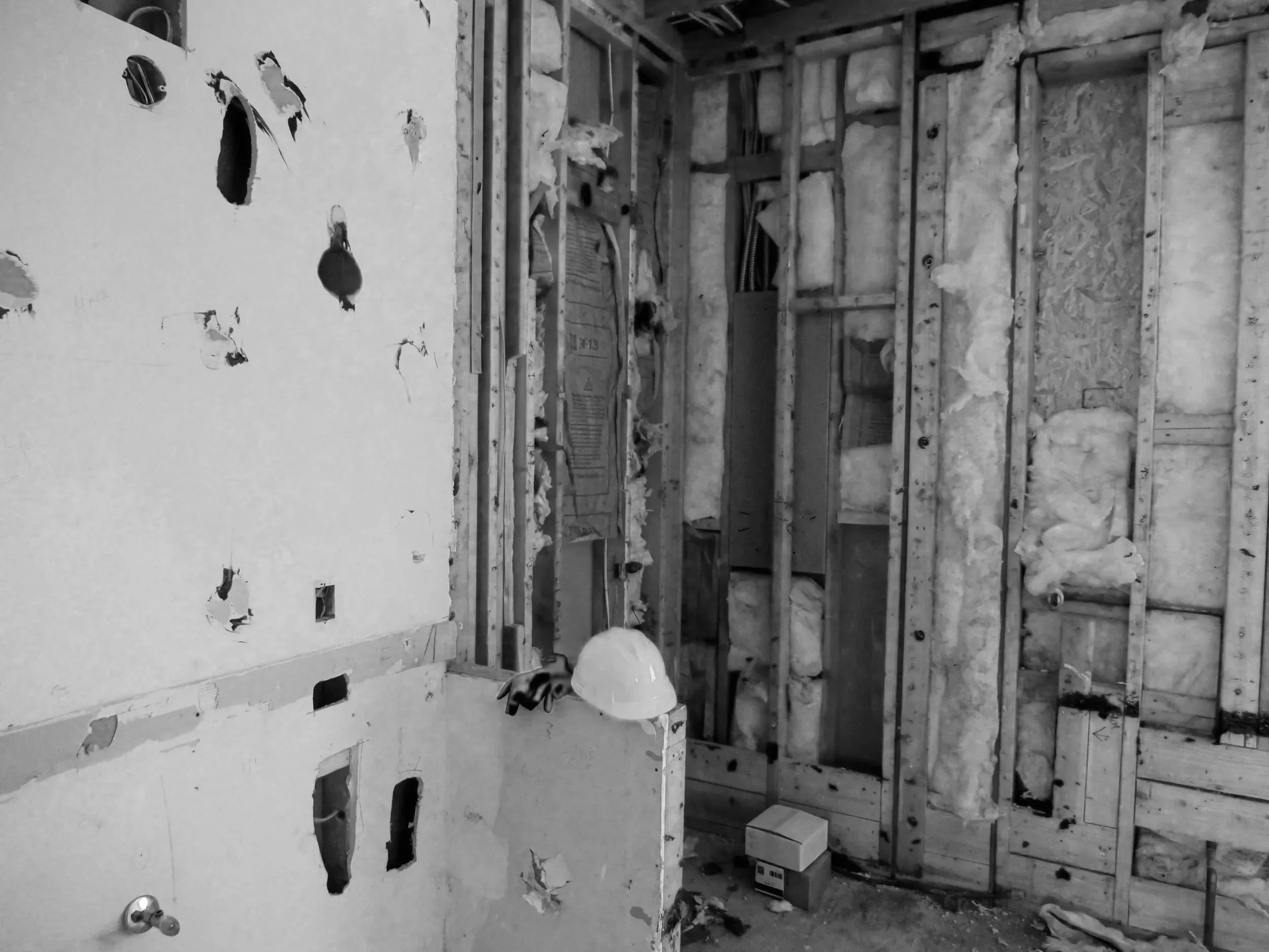 Black and white photo of exposed wall framing with insulation and electrical wiring, under construction or renovation.
