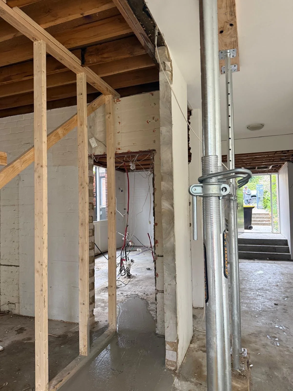 Interior of a building under renovation in Sydney with exposed wooden framing, electrical wiring, and a concrete floor. Construction supports and scaffolding are present.
