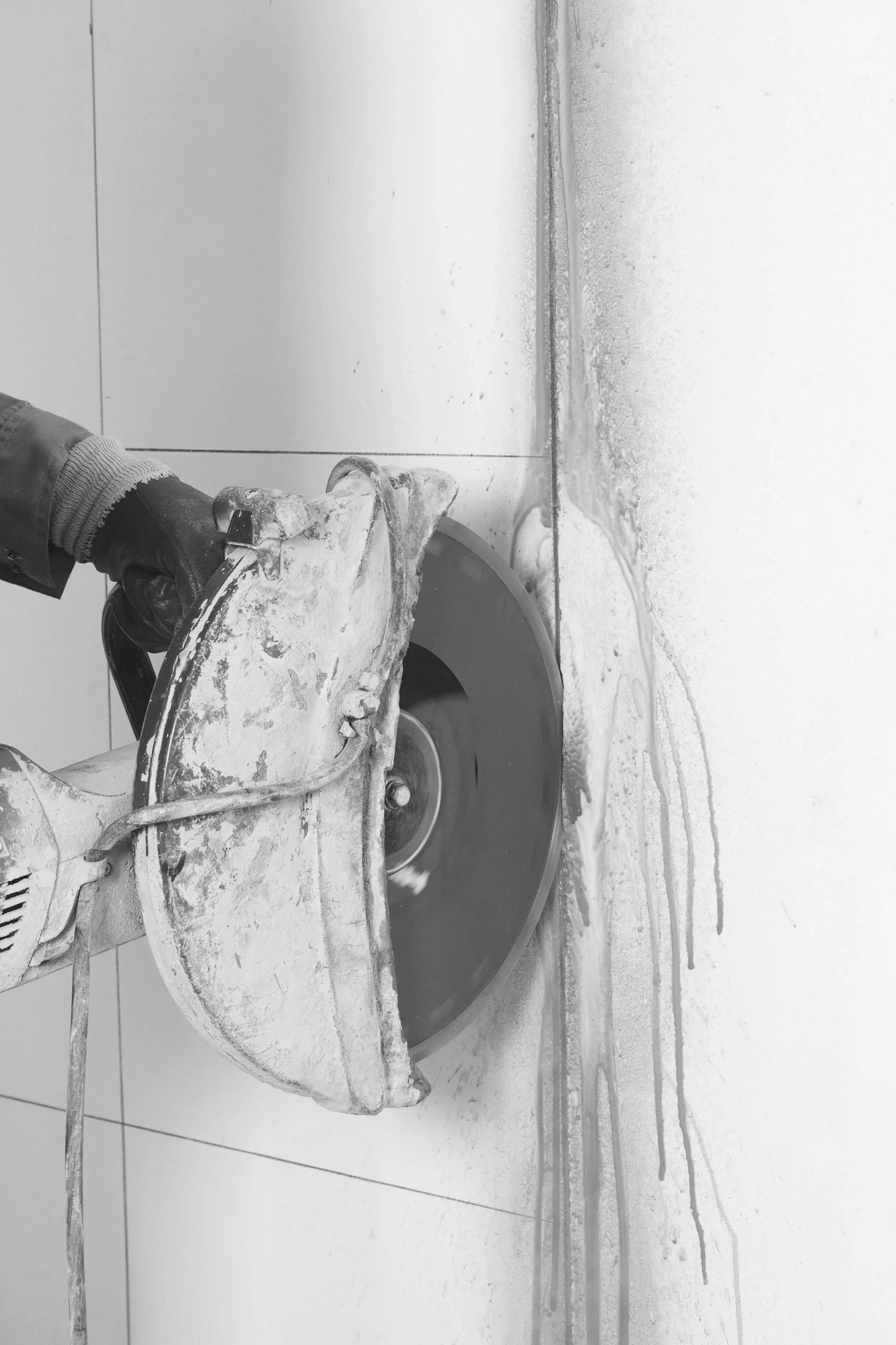 A person using a circular saw to cut through a wall or tile, with sawdust and debris around.