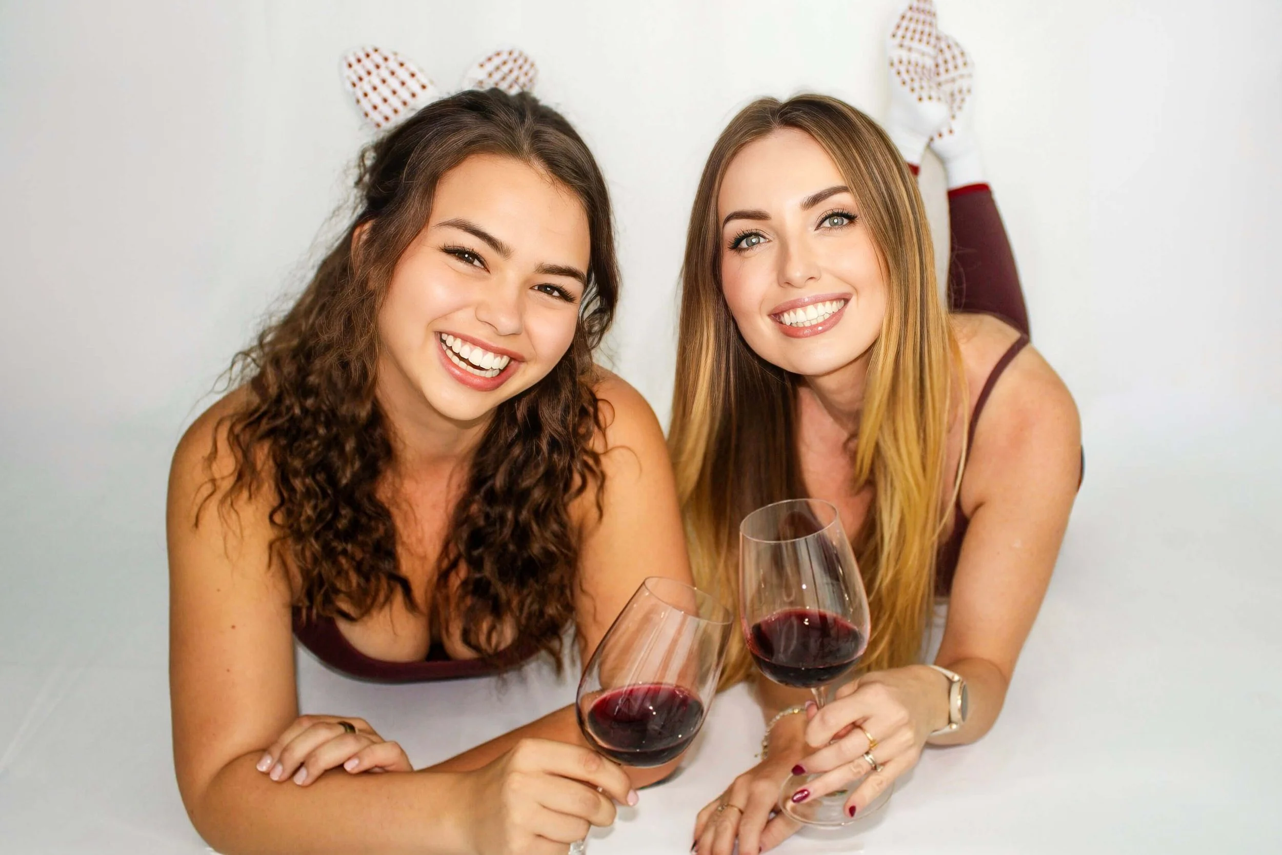 Two women holding wine glasses while showcasing Solify Pilates grip socks in a lifestyle setting.