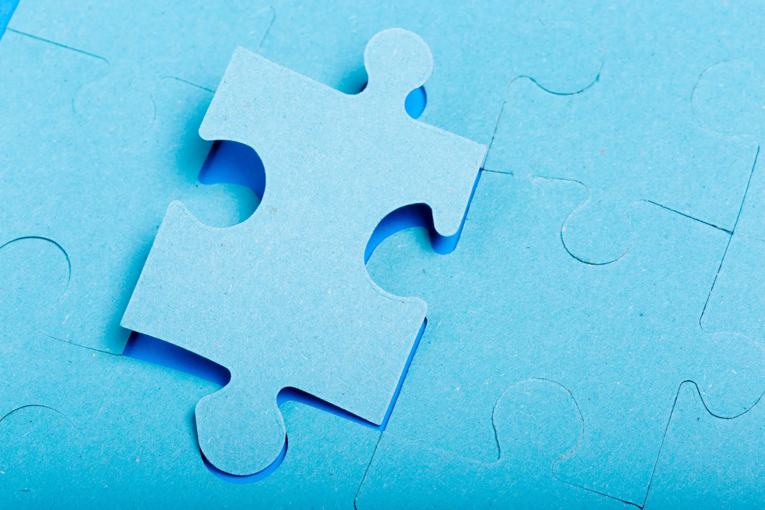 Close-up of a blue puzzle piece placed on a blue puzzle board with other puzzle pieces.