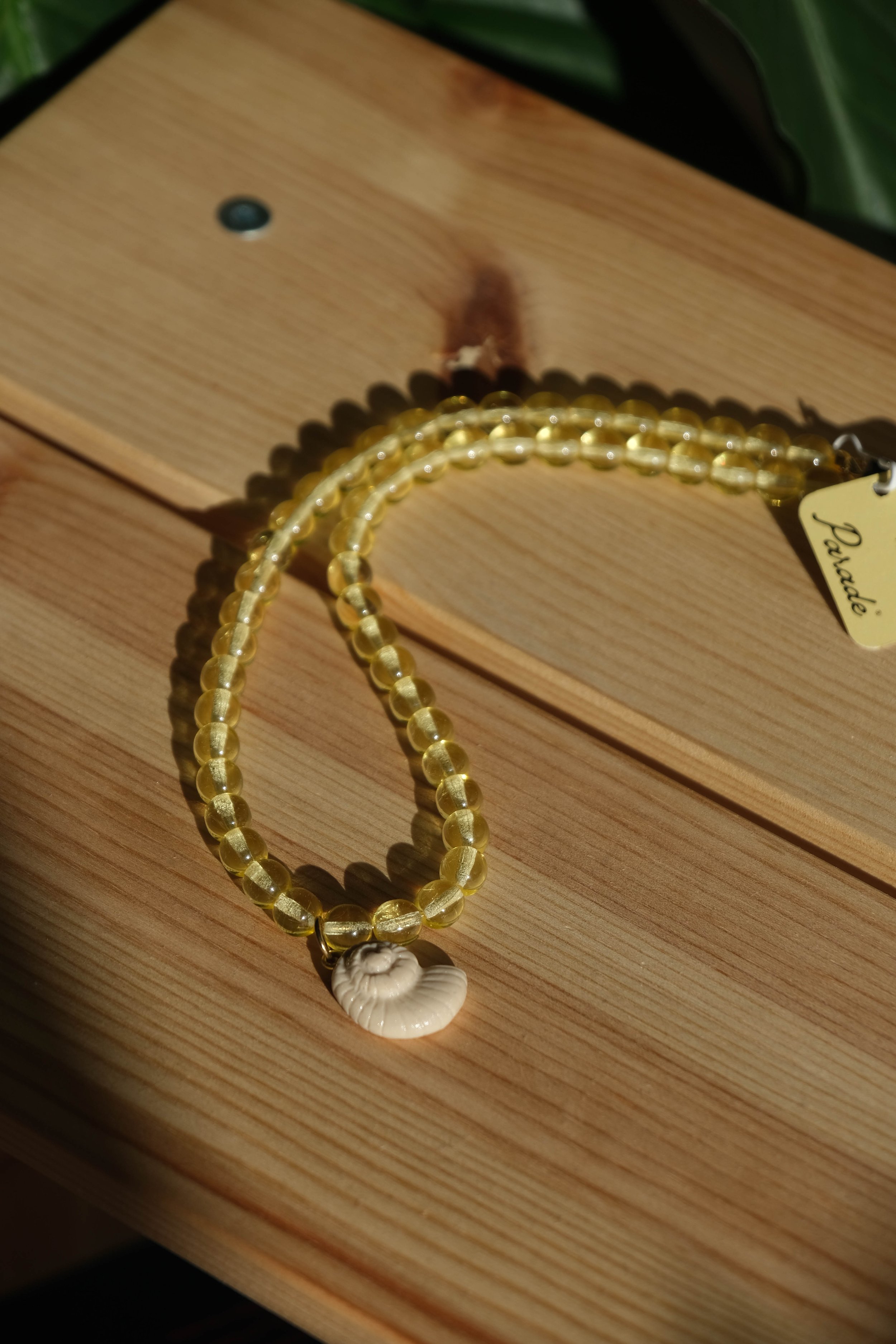 Yellow beaded necklace with a white shell pendant resting on a wooden surface.