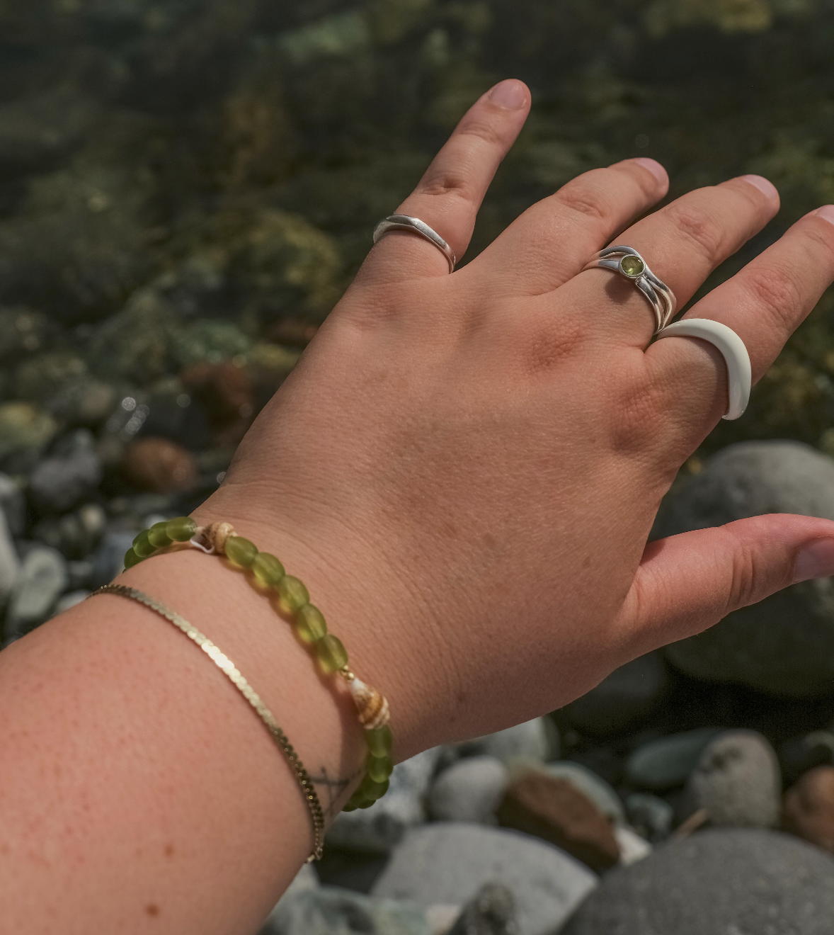 A person wearing multiple rings and bracelets holding up their hand near a rocky stream.