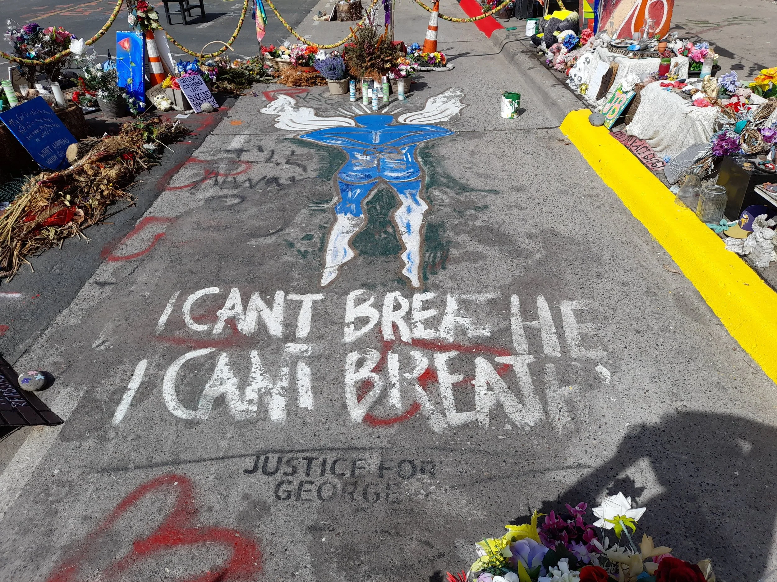 Memorial for George Floyd with a chalk-painted figure kneeling, surrounded by flowers and tributes. The sidewalk reads, "I CAN'T BREATHE," and "JUSTICE FOR GEORGE."