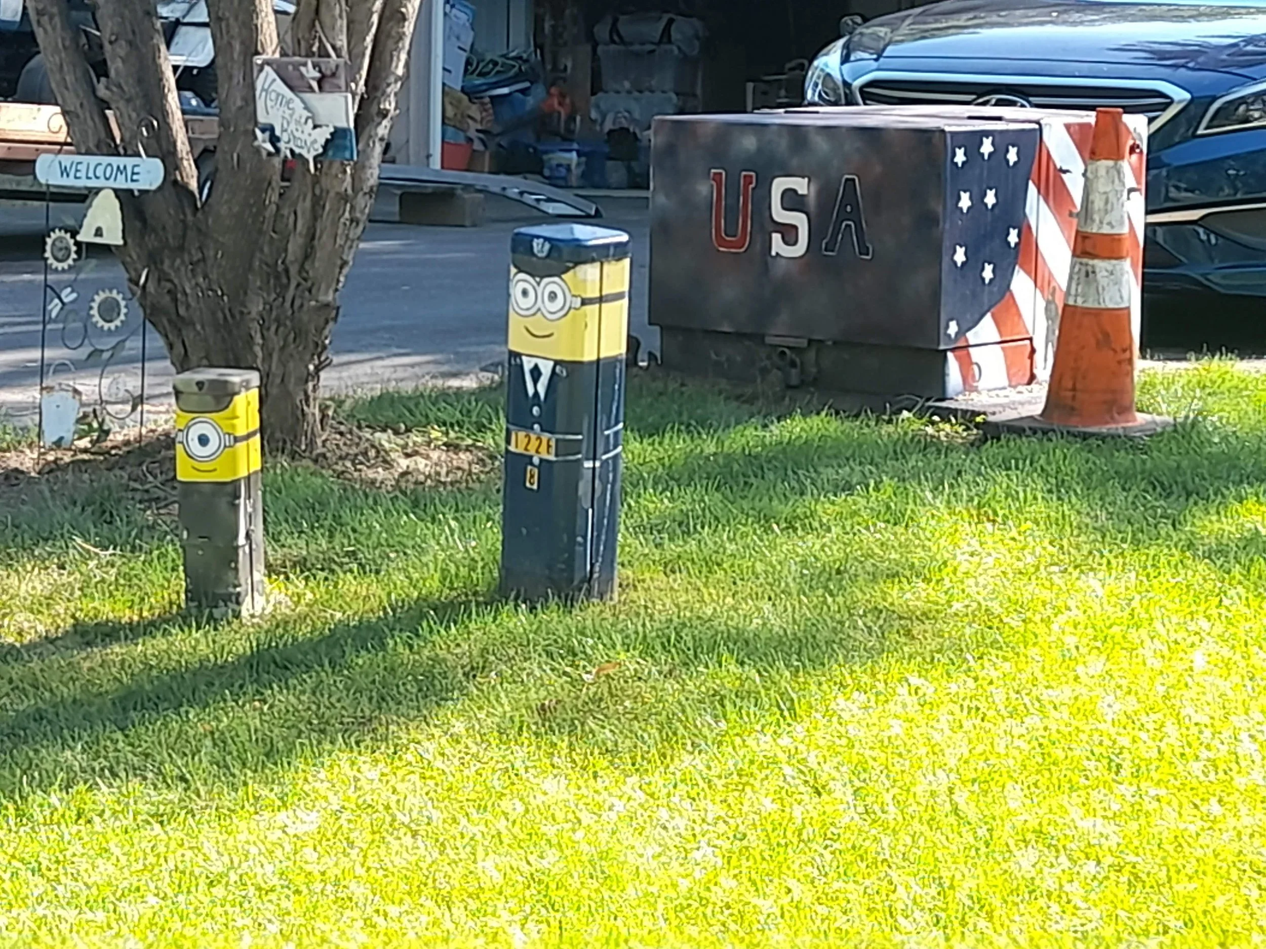 Decorative items with a theme of the United States, including a mailbox with Minions, a flag, and a traffic cone, near a tree.