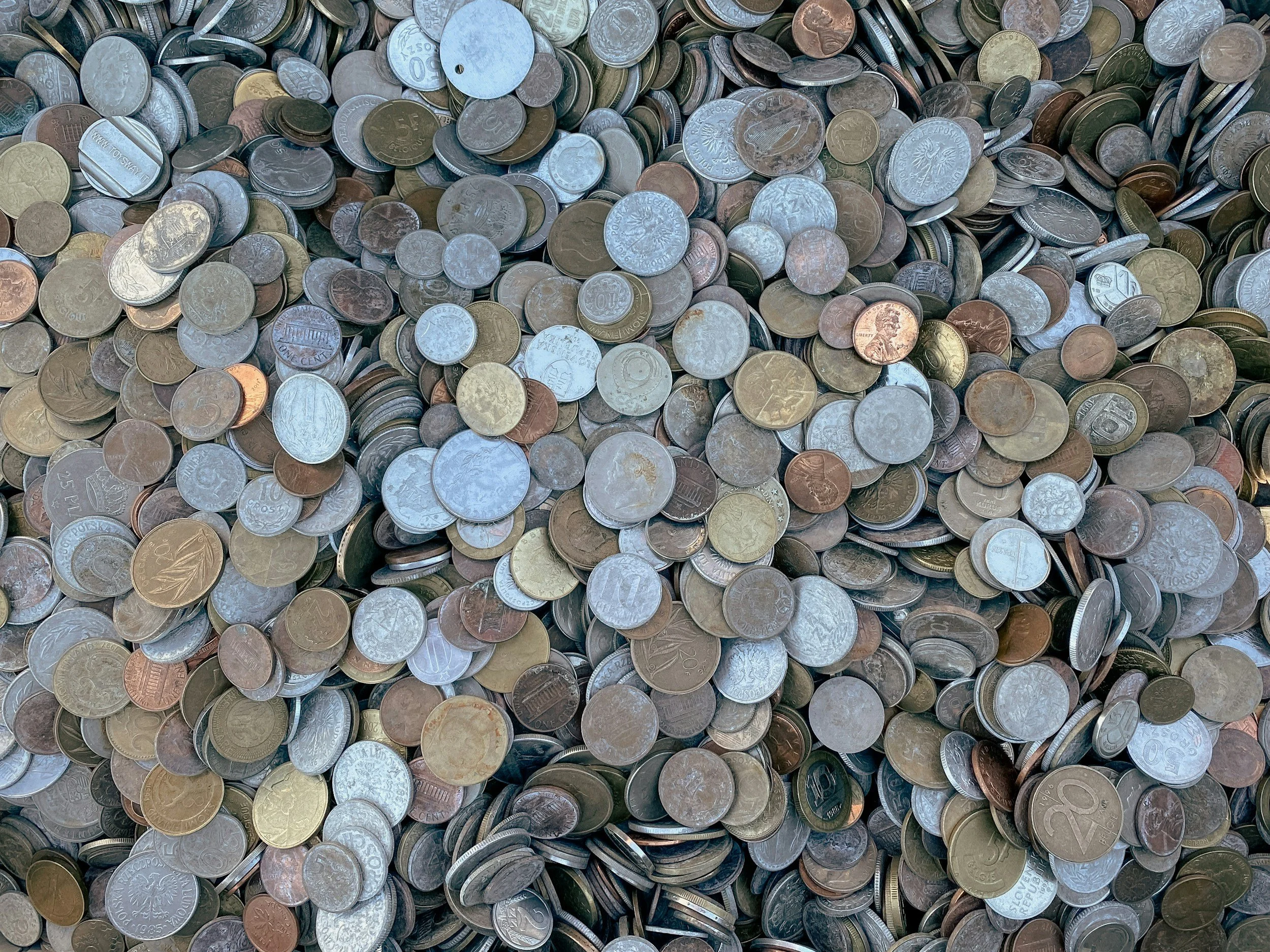 A large collection of scattered coins of various denominations and currencies, including pennies, nickels, dimes, and quarters.