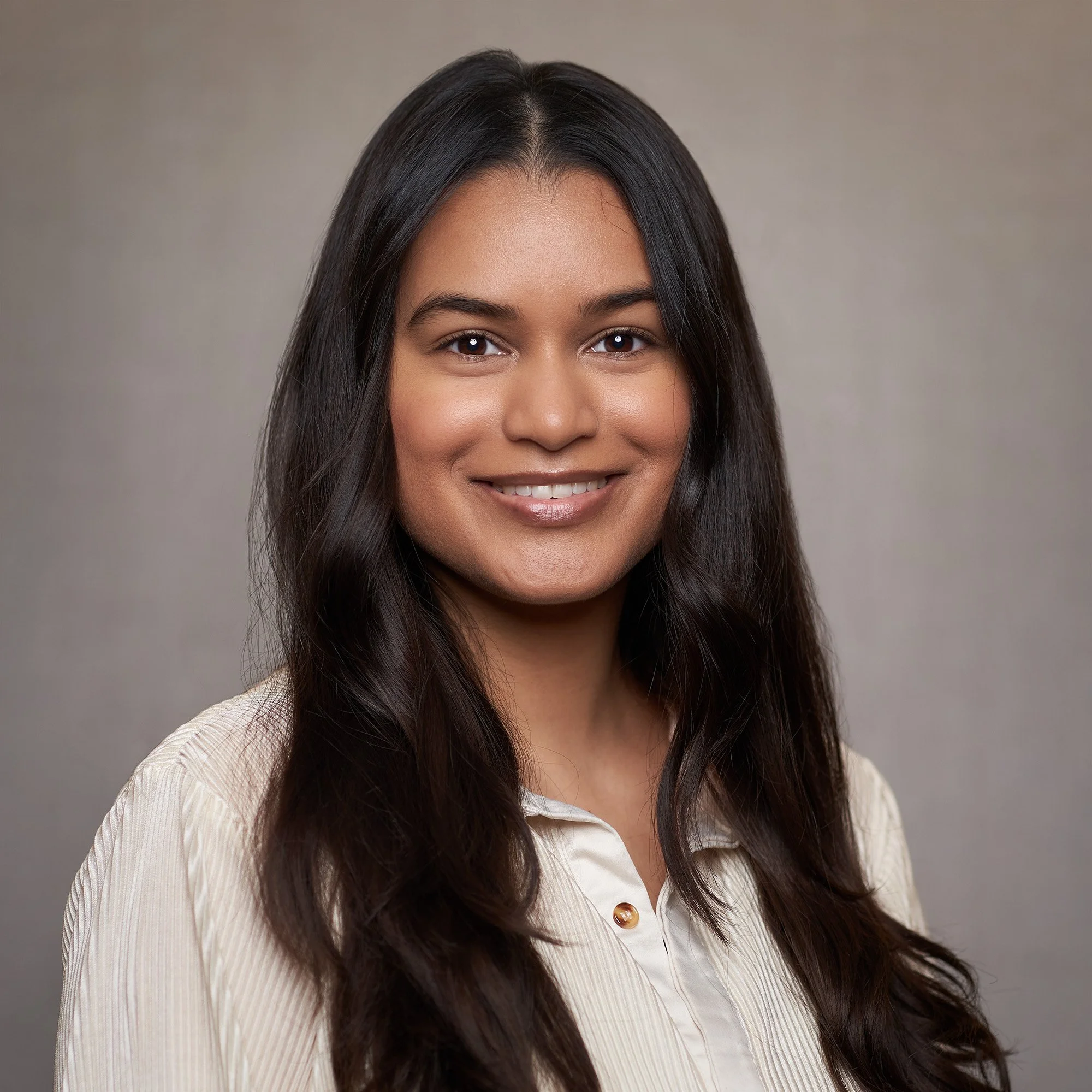 A young woman with long dark hair smiling at the camera, wearing a light-colored collared shirt.