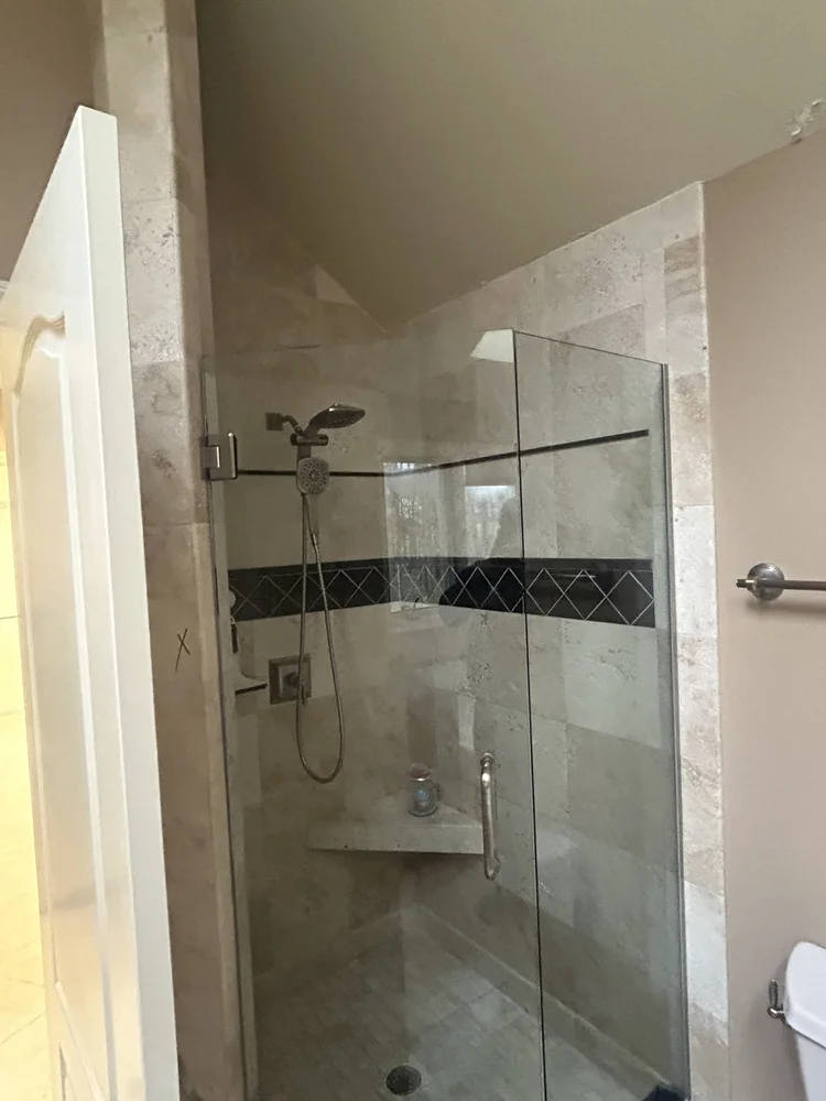 Bathroom shower with glass enclosure, beige tiled walls, black decorative tile band, and a showerhead on a chain.