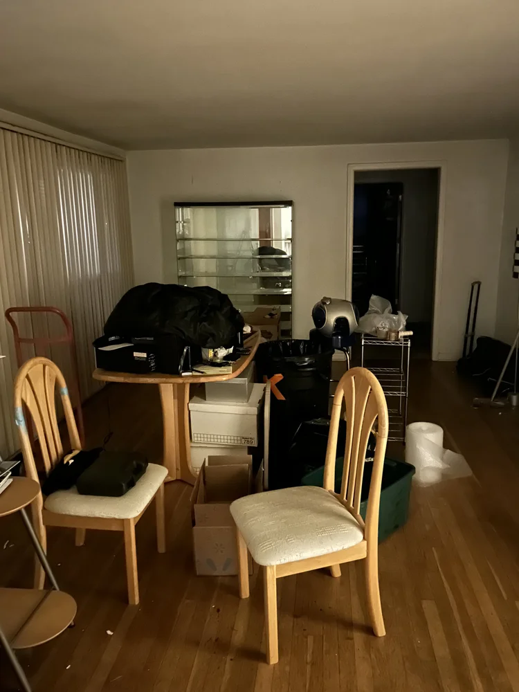 Living room with chairs, a table, and various household items and boxes.