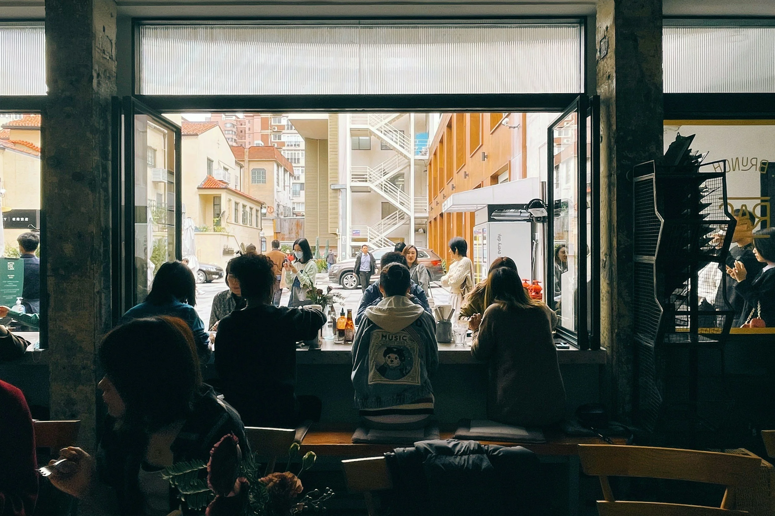 People sitting at a cafe counter facing the window, with more people outside on the street.