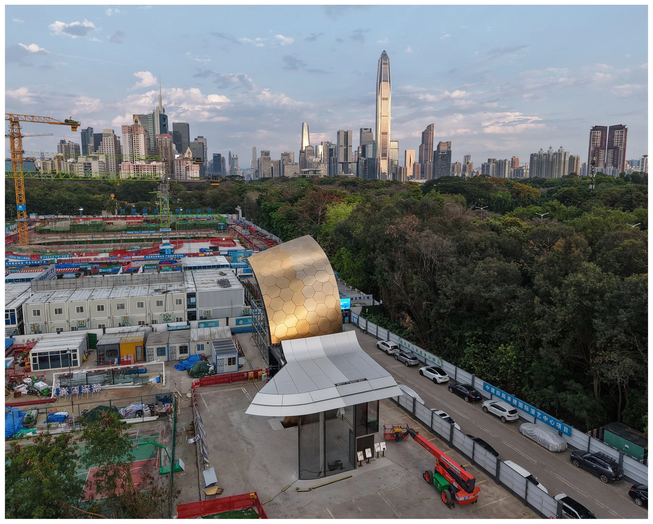 Cityscape featuring a park with dense trees and a modern skyline in the background, including the distinctive vertical skyscraper, with construction sites and temporary structures in the foreground.