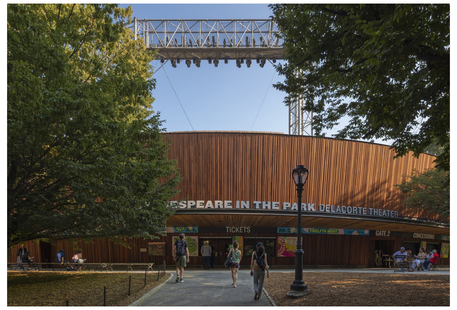 People entering the Delacorte Theater with a sign reading 'Shakespeare in the Park' in Central Park, New York, during daytime.
