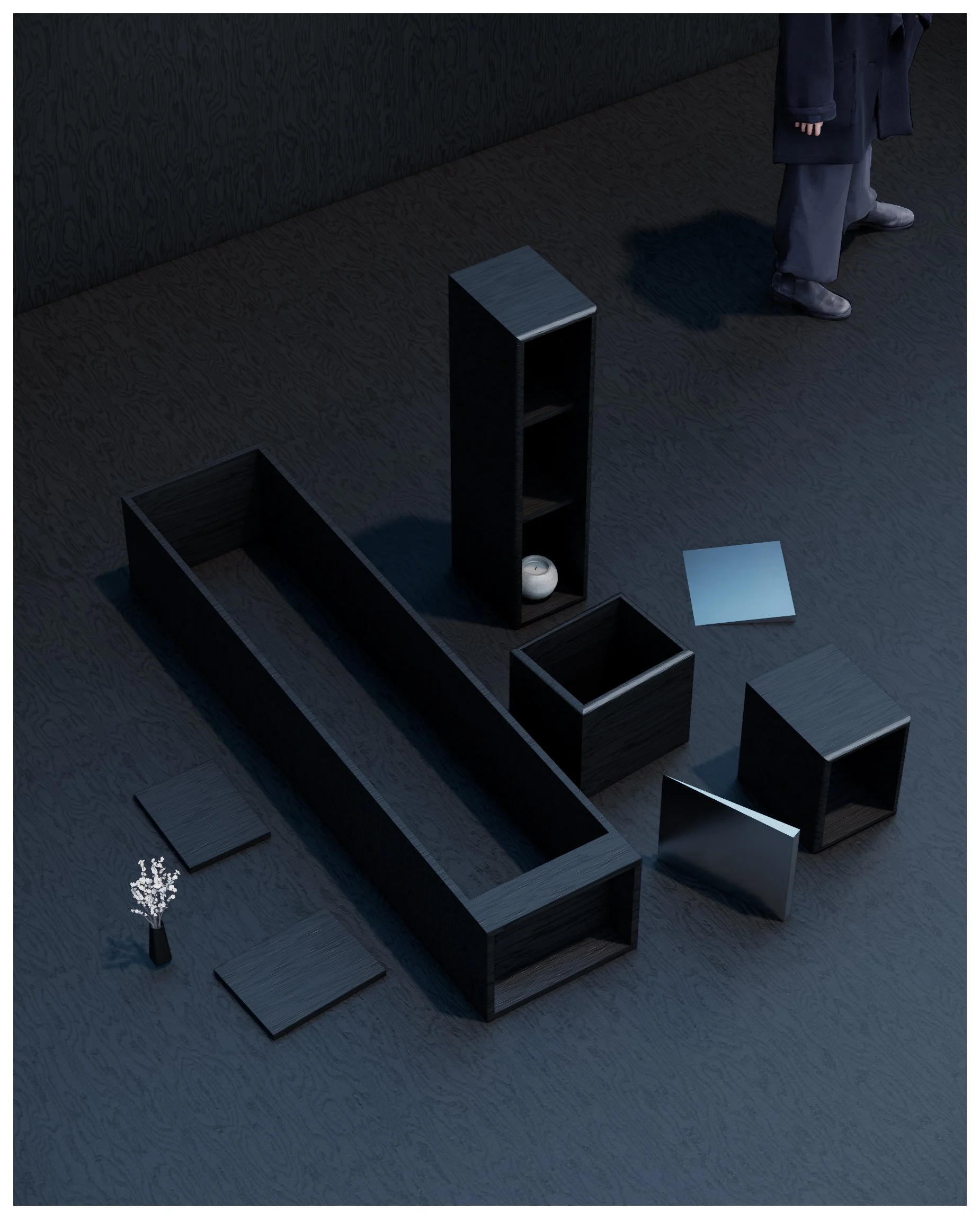 Top-down view of modern black furniture pieces arranged on a dark wooden floor, including shelves, a small table, and decorative objects, with a person standing in the background.