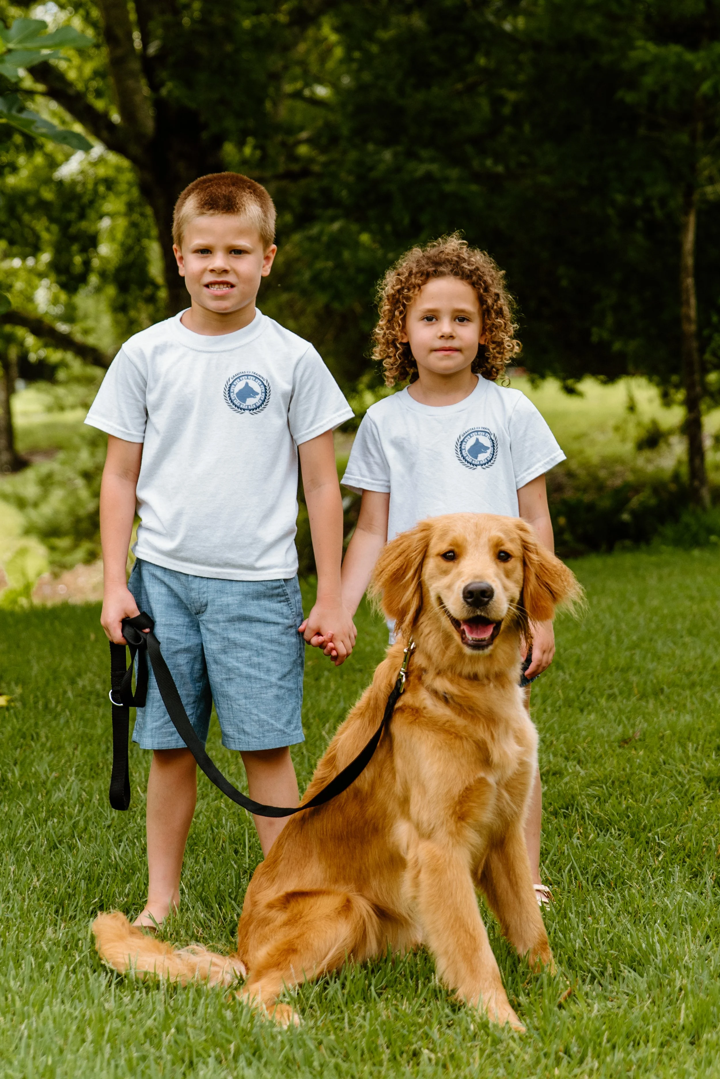 Two children holding hands with a golden retriever dog in a park.