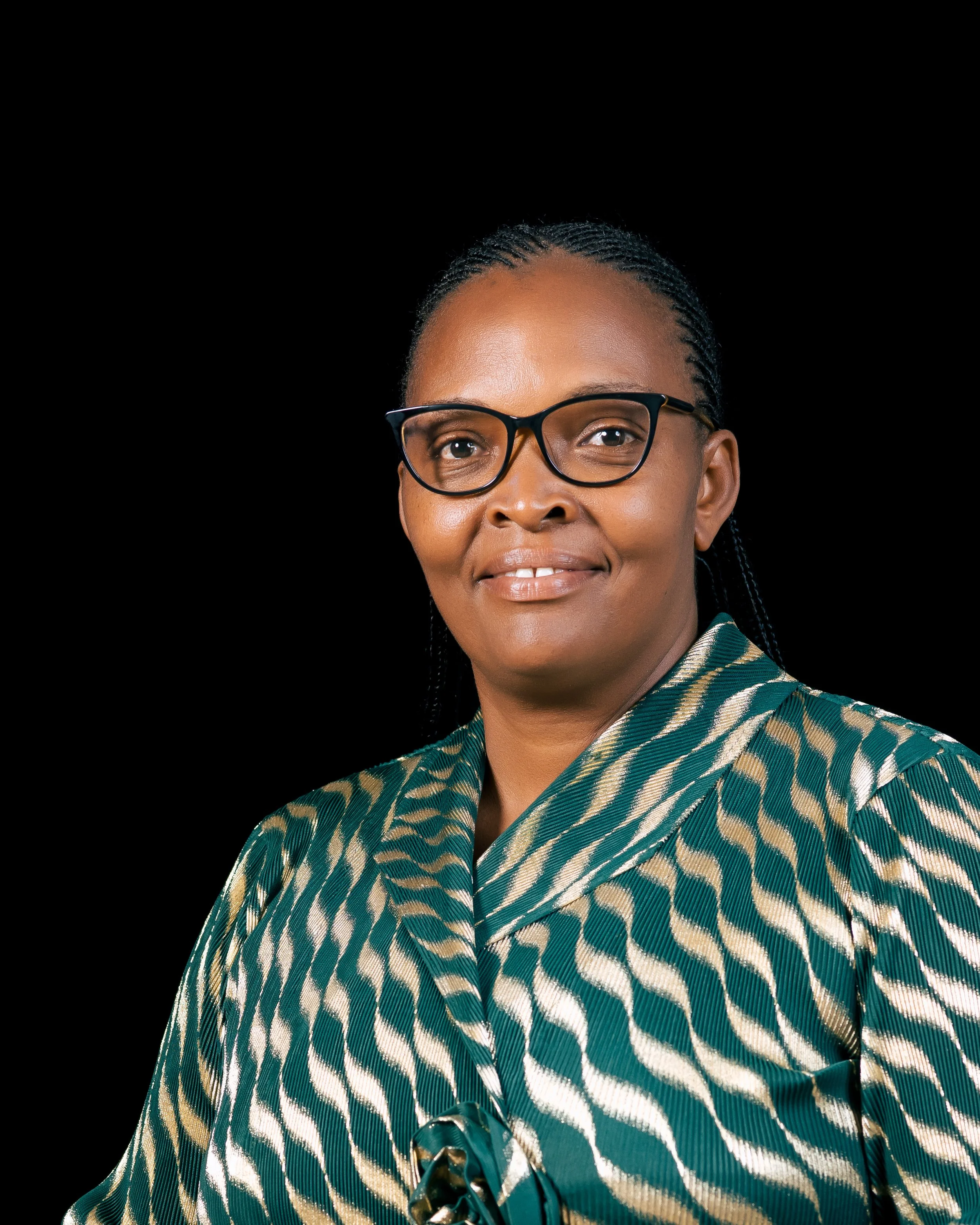 Portrait of a woman wearing glasses and a patterned green and beige outfit, smiling, against a black background.