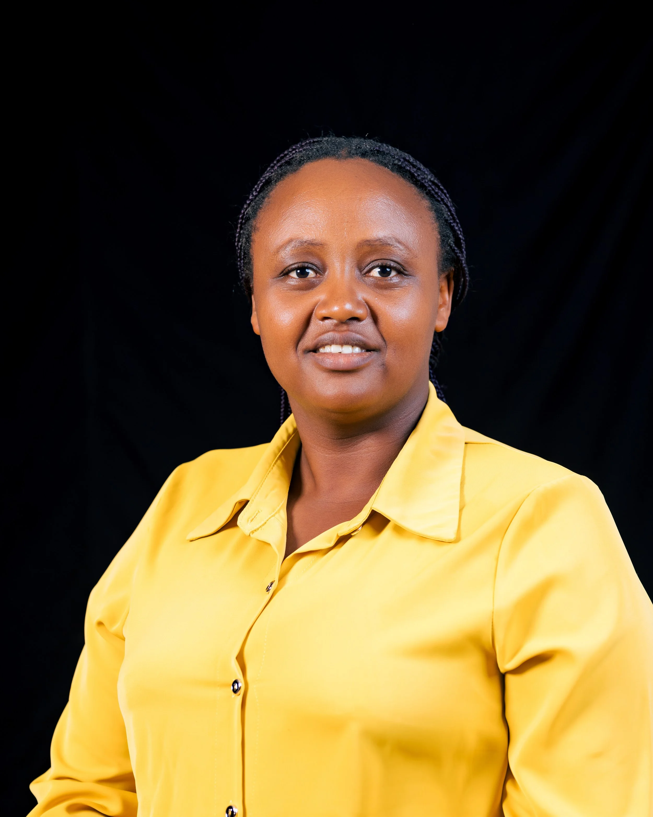 Close-up of African American woman with braided hair wearing a yellow blazer against a black background.