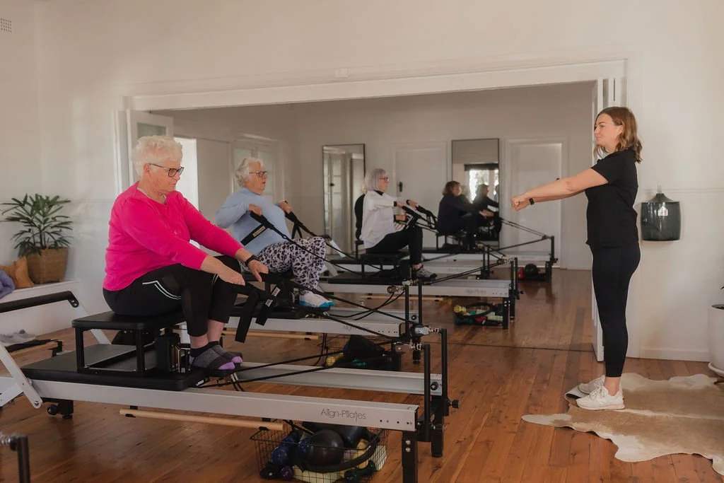 Instructor leading a group of senior women in a seated rowing workout in a living room.