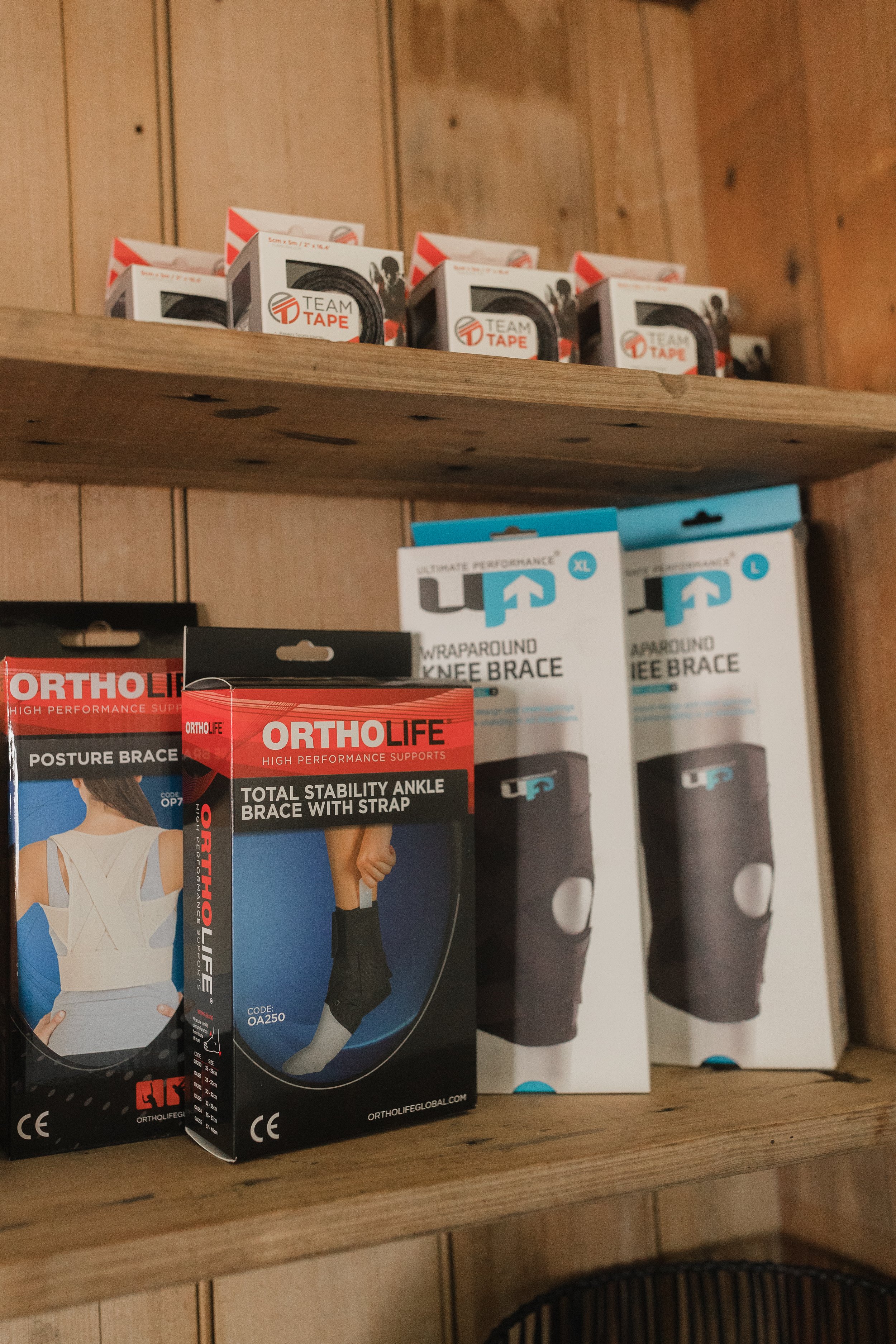 Shelf with boxes of orthopedic supports, including ankle braces and knee braces, in a wooden cabinet.