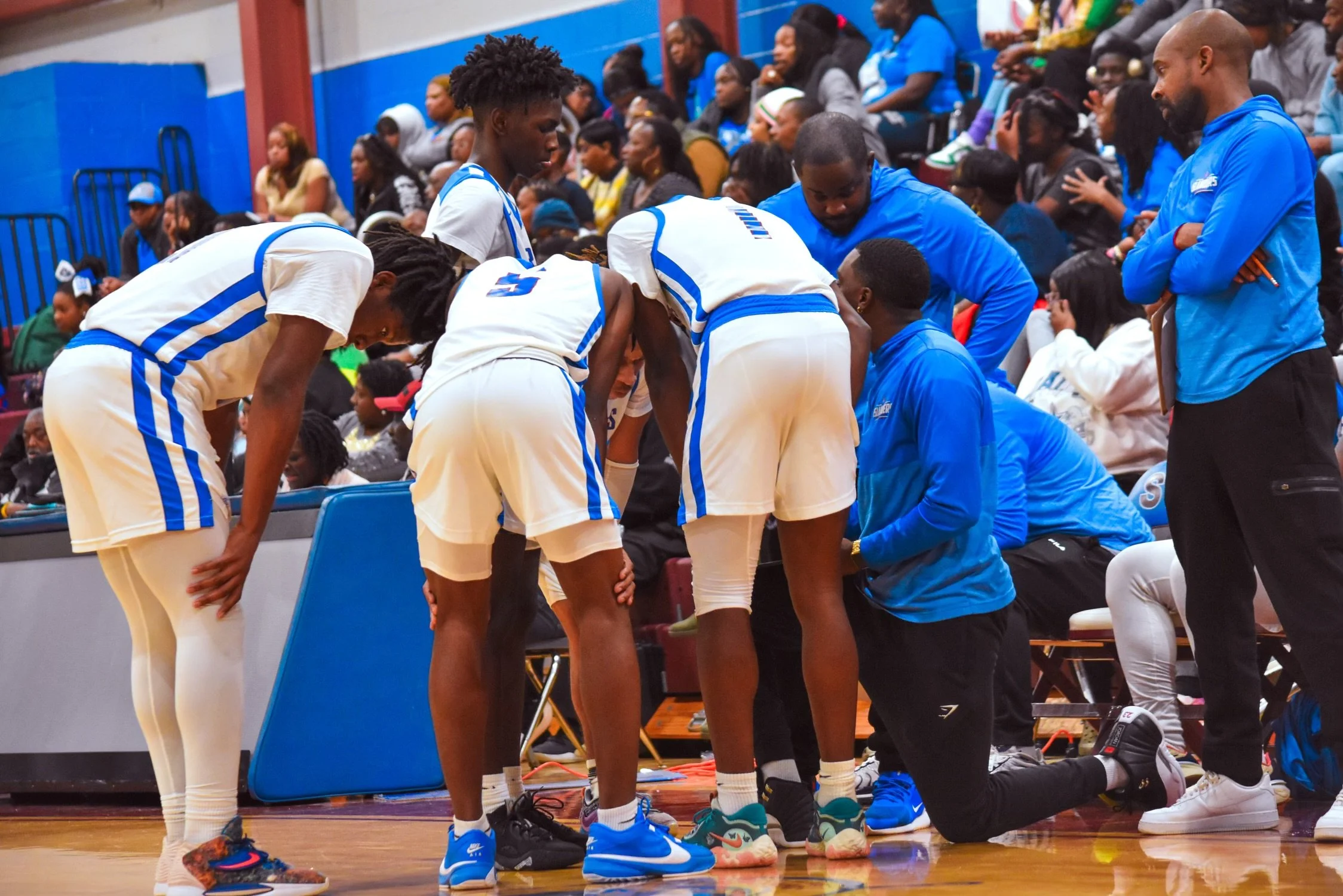 Basketball players huddled with coaches during a game in a gymnasium.