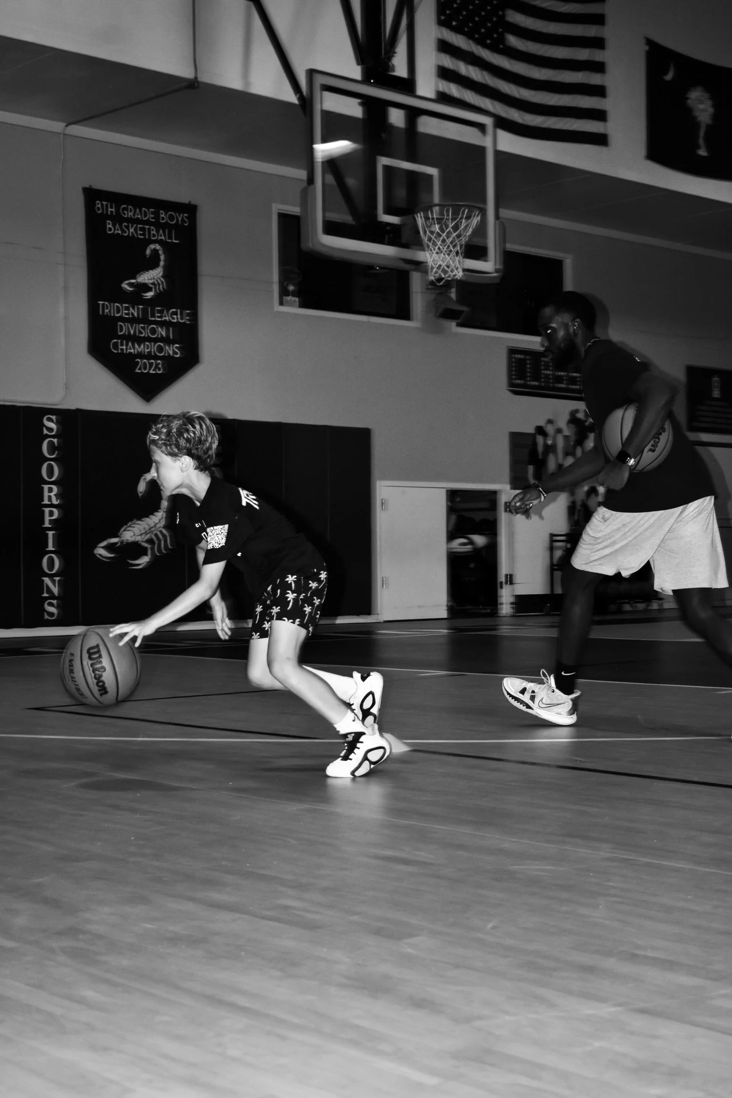 A young boy dribbling a basketball on an indoor basketball court with an adult man guarding him.