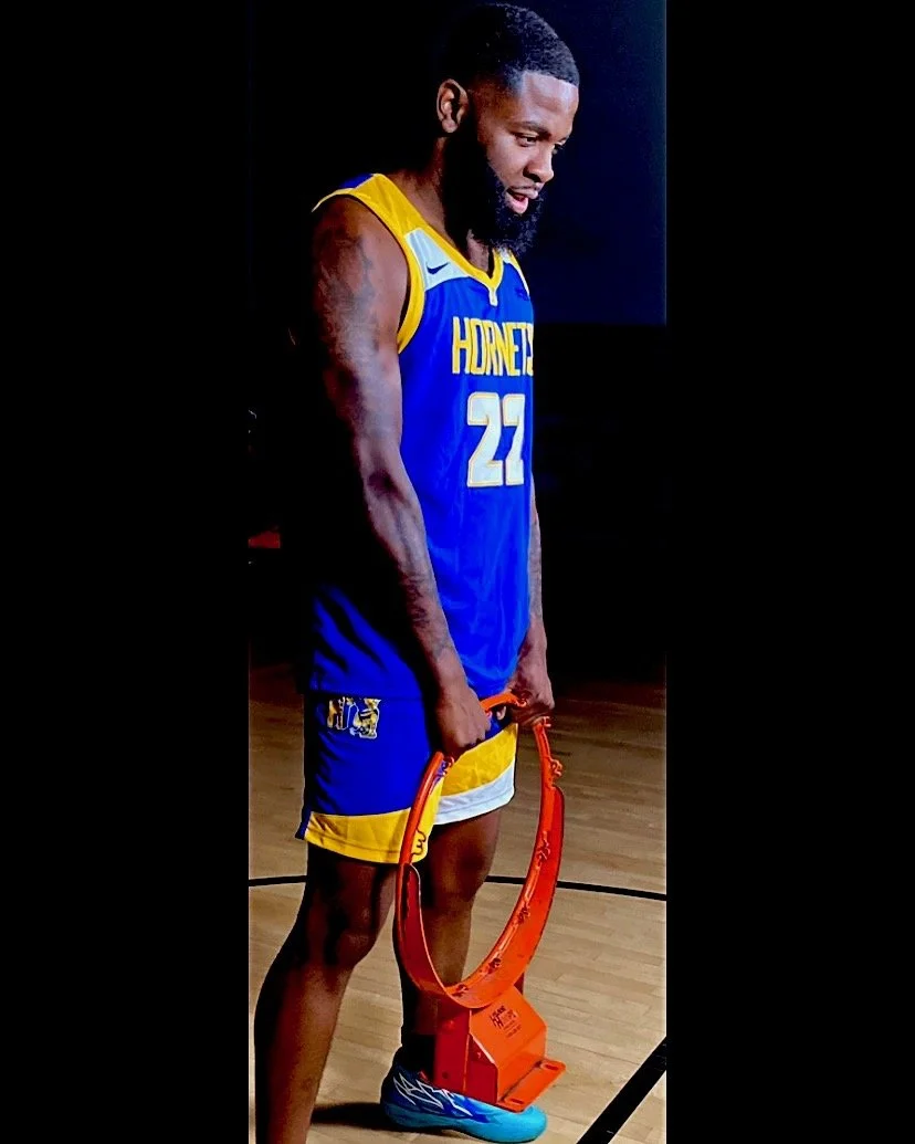 A male basketball player in a blue and yellow jersey with the number 22, holding a trophy, standing on a basketball court.