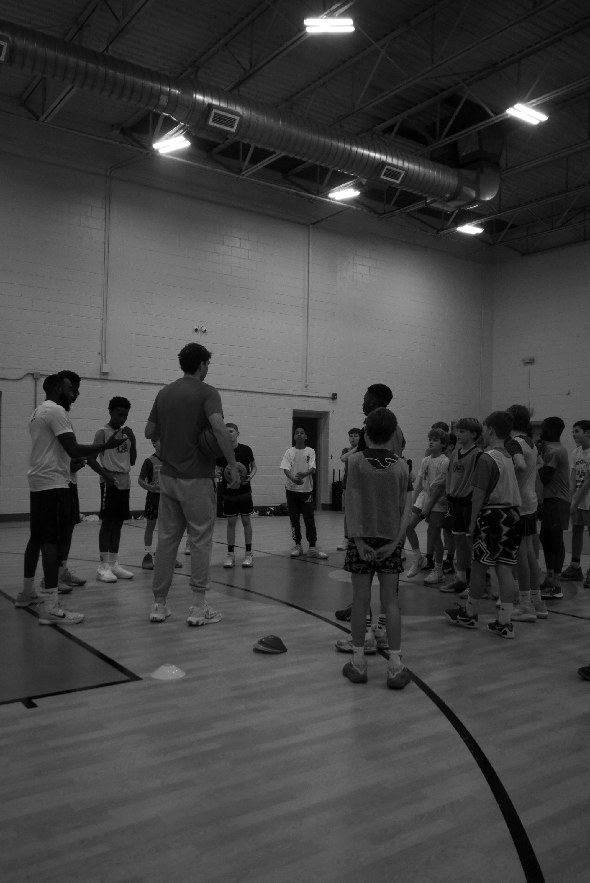 A coach giving instructions to a group of young basketball players in a gymnasium.