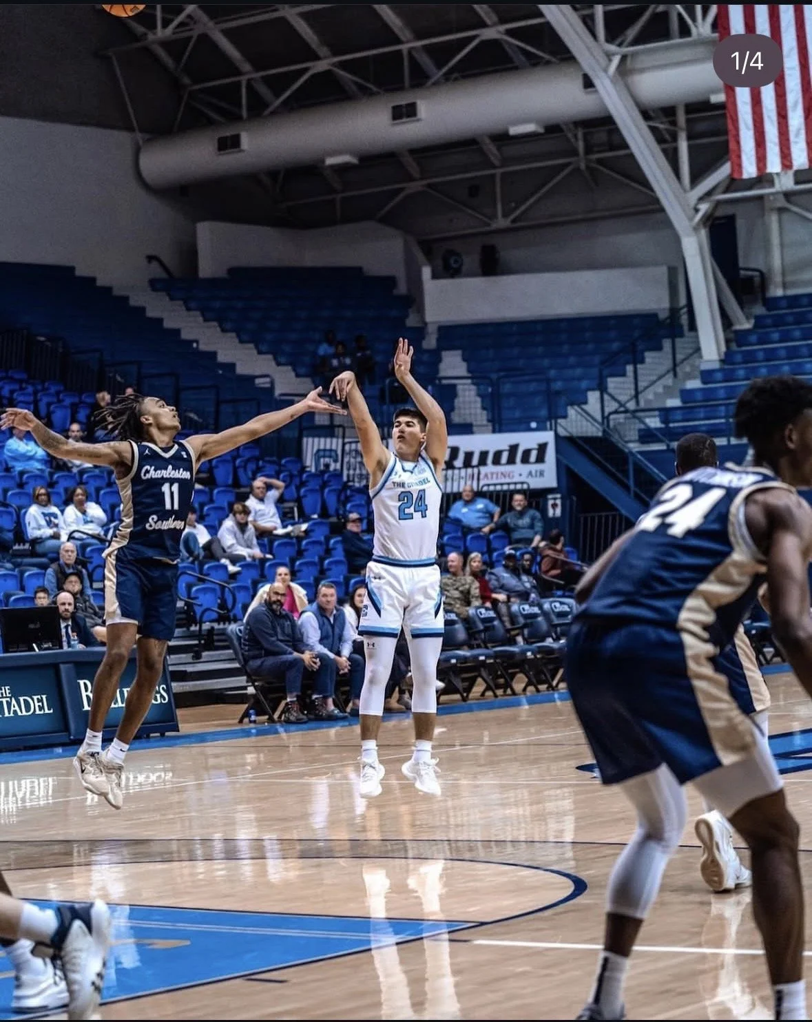 A basketball game with players in blue and white uniforms playing on the court, with spectators seated in the background.