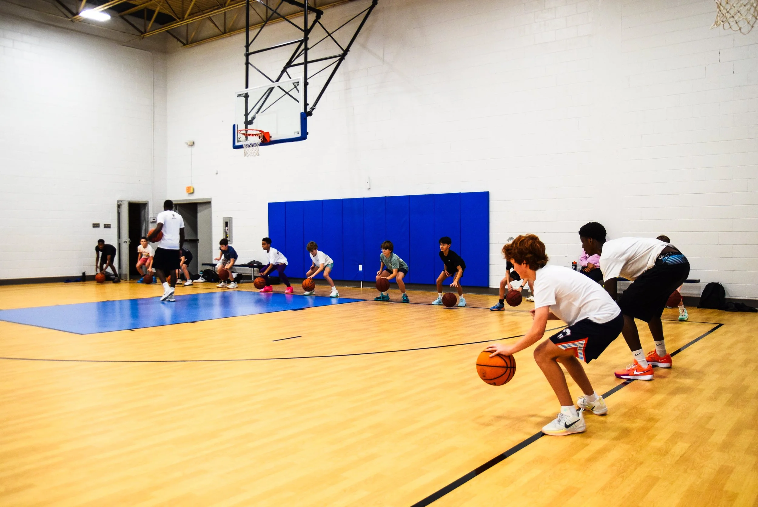 Young children participating in a basketball drill with coaching staff in an indoor gymnasium.