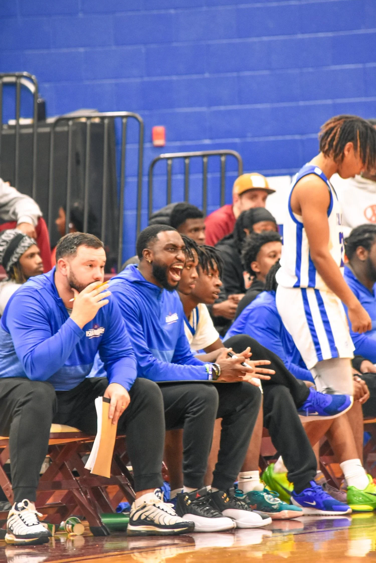 Basketball players and coaches sitting on the bench during a game, with one player standing and the coaches reacting enthusiastically.