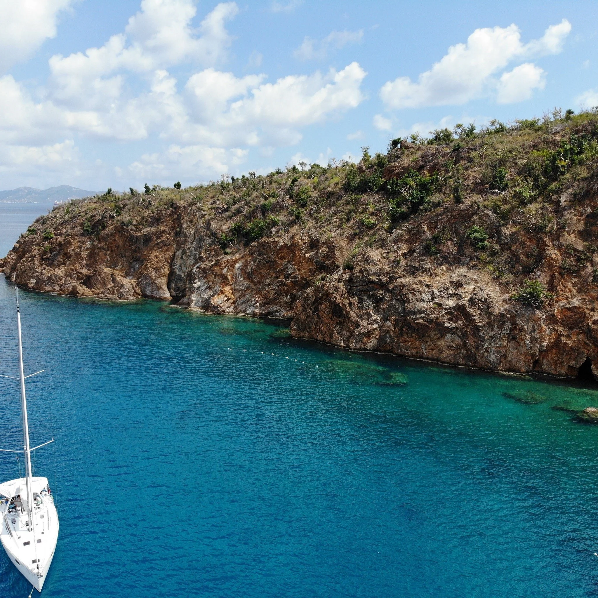 A boat floating near a rocky coastal cliff under a partly cloudy sky.
