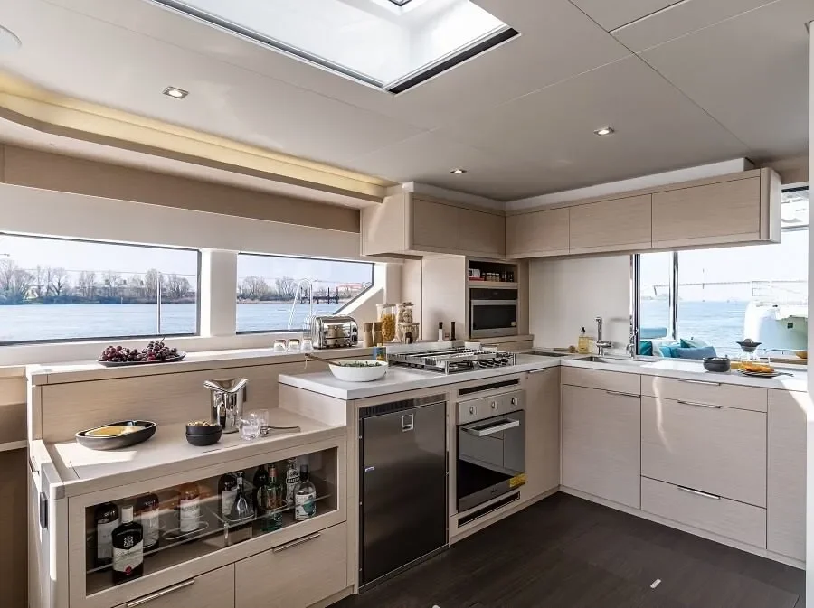 Modern kitchen with light wood cabinets, stainless steel appliances, and a view of water through large windows.