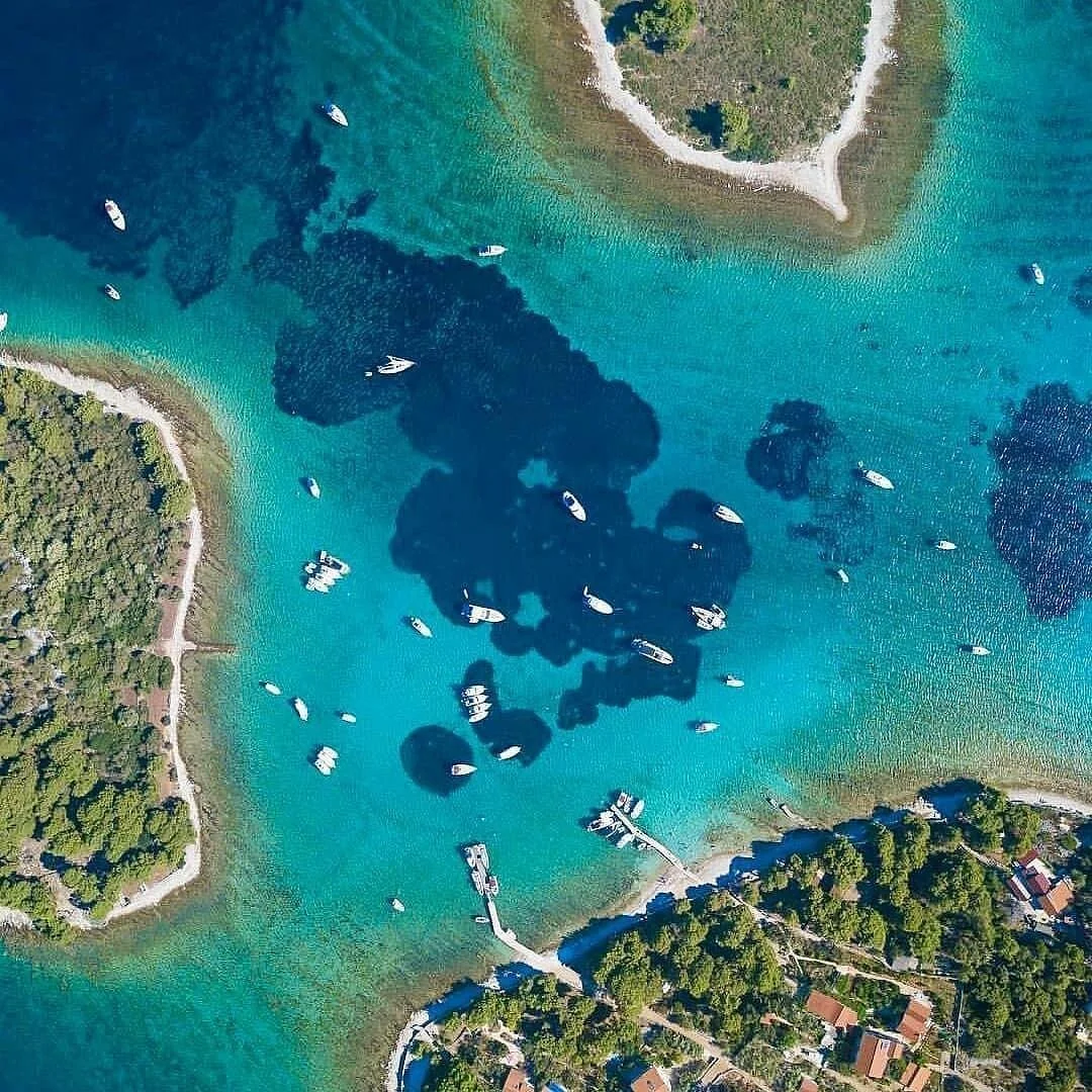 Aerial view of a coastal area with clear blue water, small islands, many boats, and green trees along the shore.