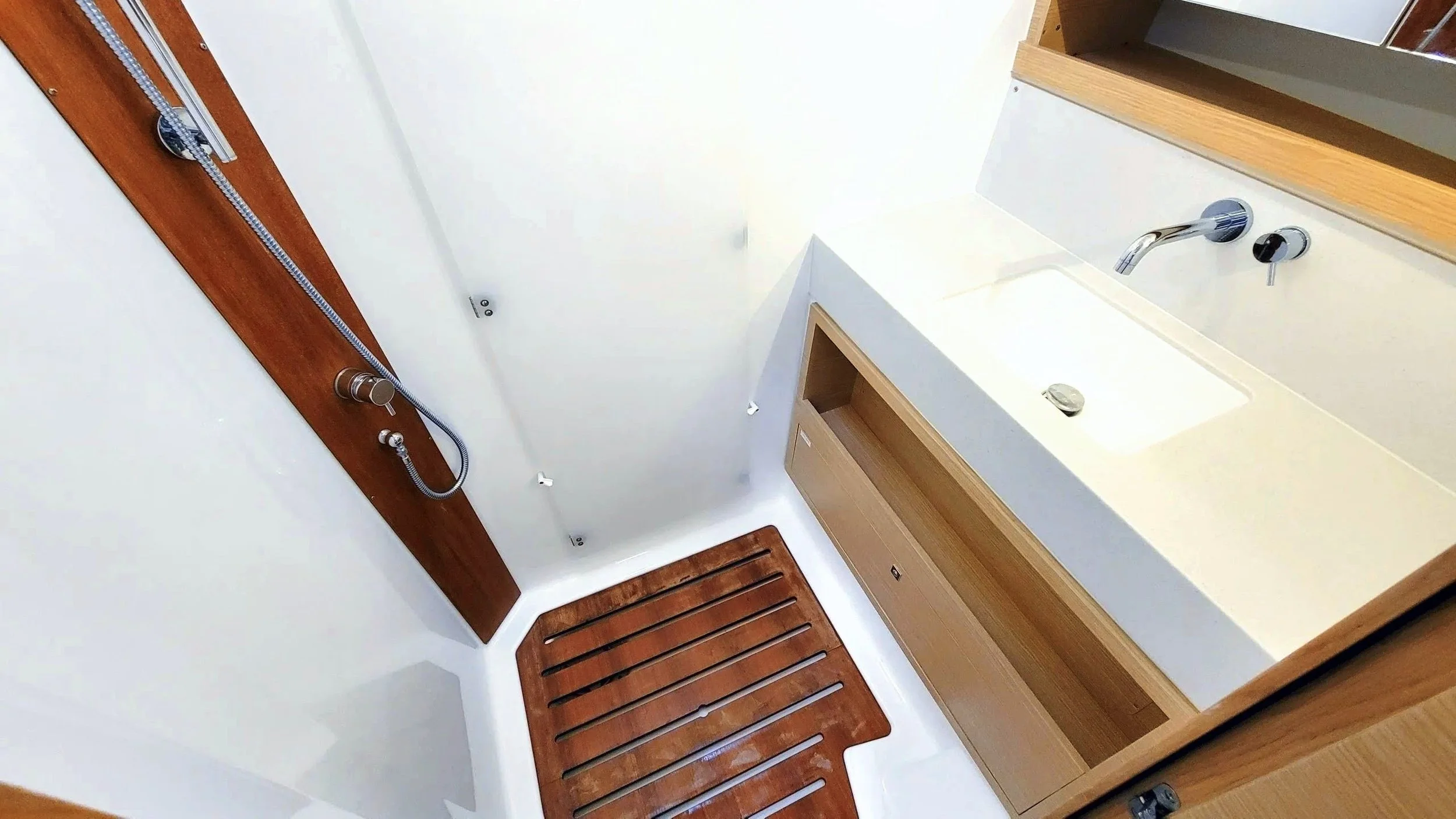 Modern bathroom with white walls, wooden floor mats, a white sink with a wooden cabinet, and a wall-mounted shower head with a wooden panel.
