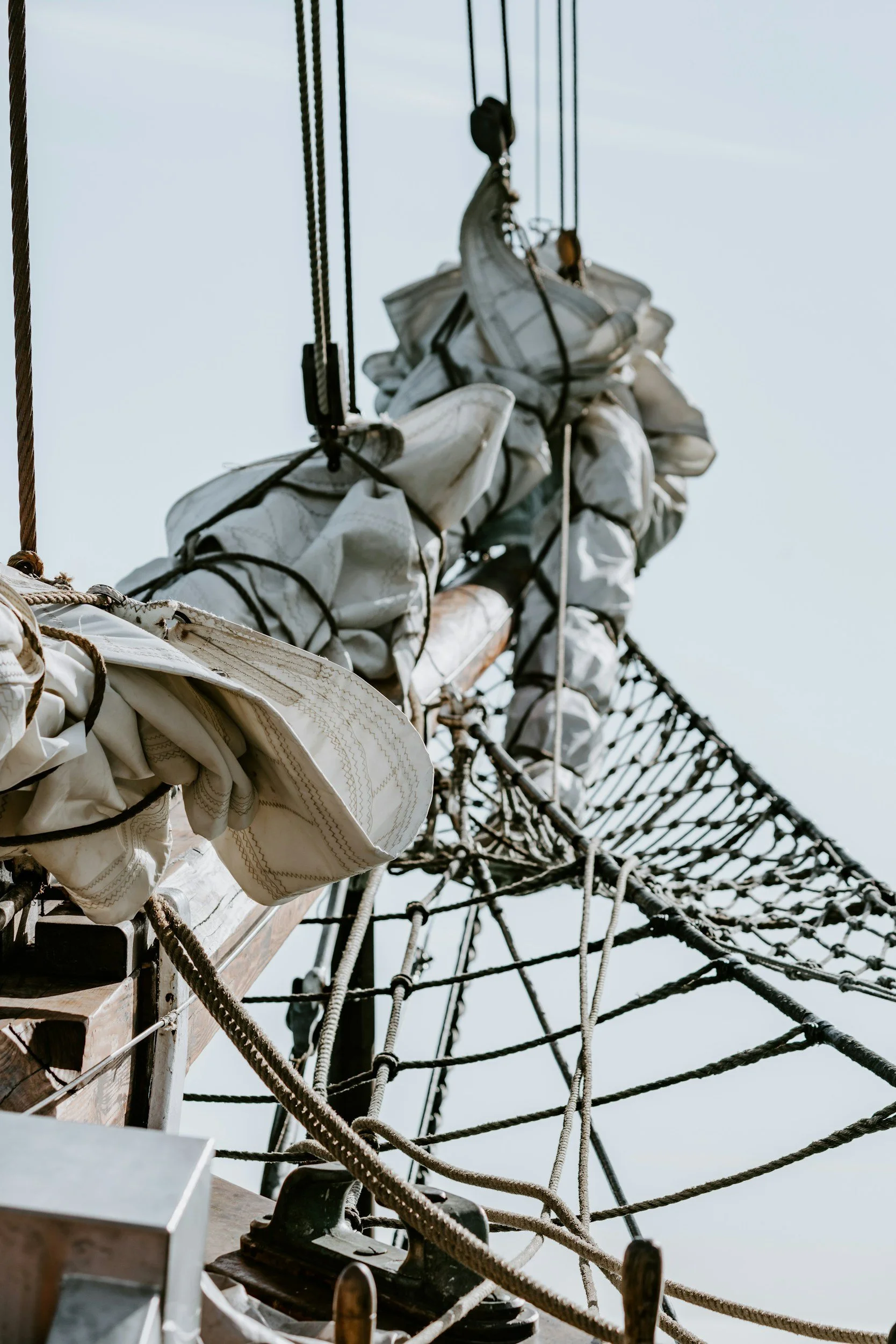 Close-up view of the tall ship's rigging and folded sails against a light sky.