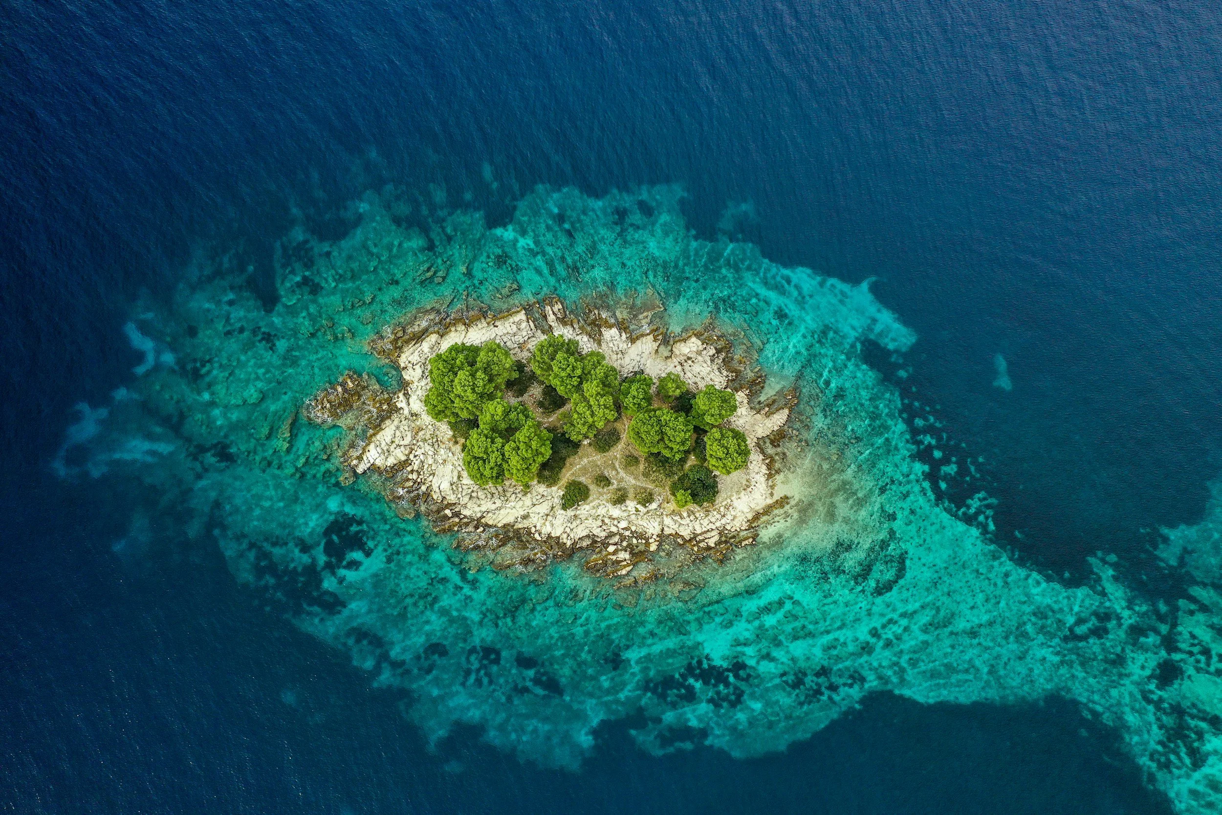 Aerial view of a small rocky island with green trees, surrounded by turquoise water in Croatia's Adriatic sea.