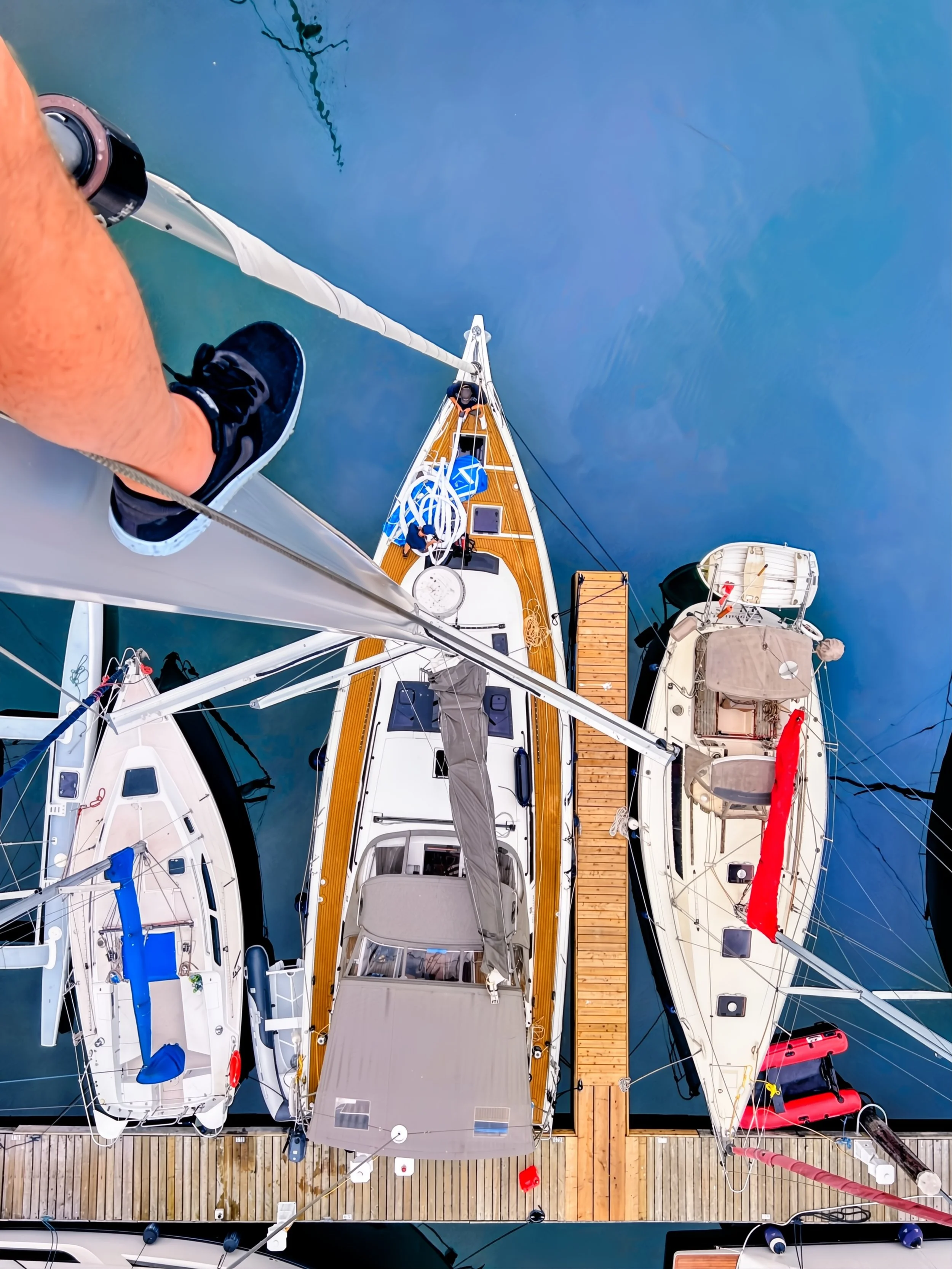 Aerial view of three sailboats docked at a marina, viewed from above, showing the decks and masts.