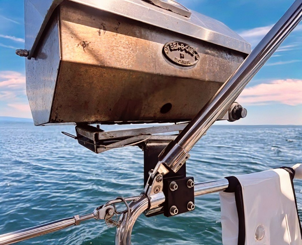 Close-up of a stainless steel grill mounted on a boat with the ocean and a partly cloudy sky in the background.