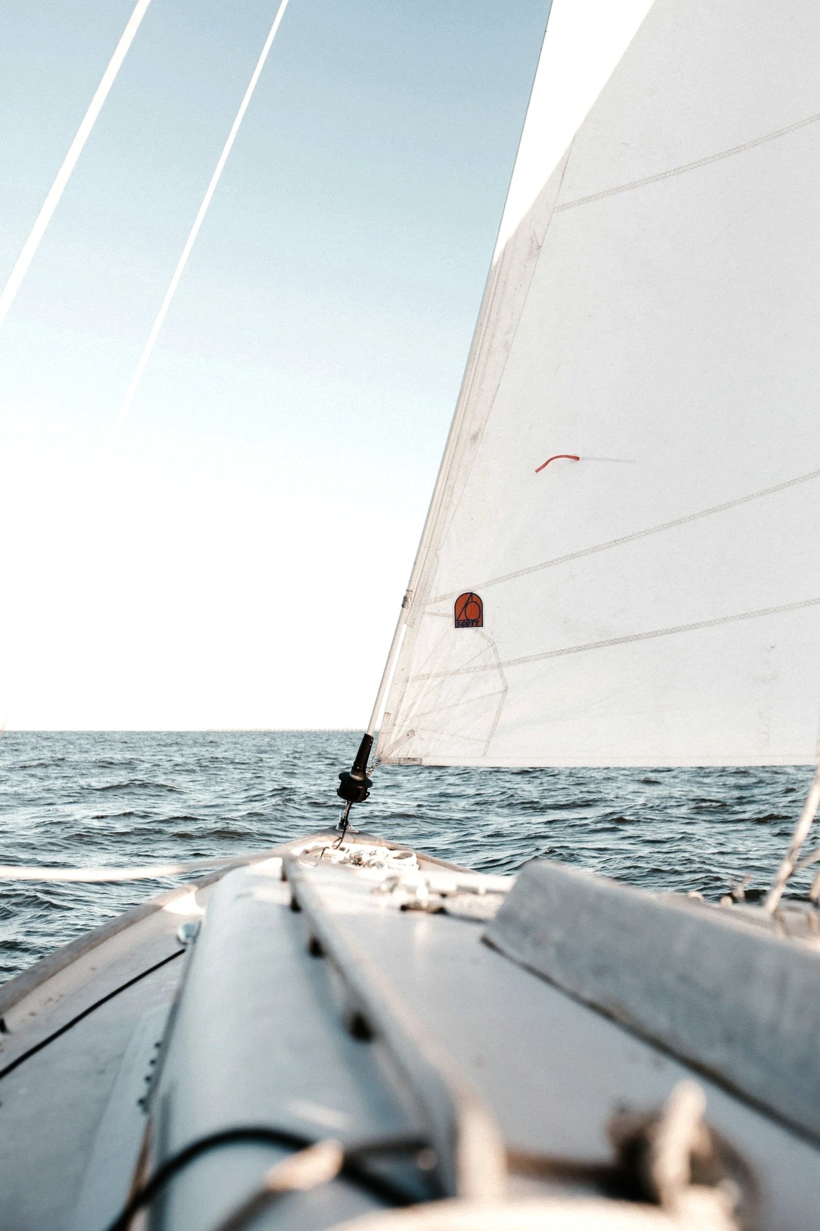 View from a sailboat showing the boat's bow, with a sail and the open ocean in the background.