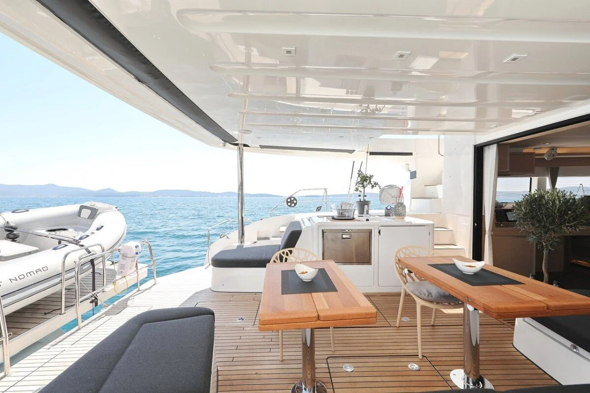 Outdoor dining area on a yacht with a view of the ocean, tables with bowls, a kitchenette, and a nearby inflatable boat.