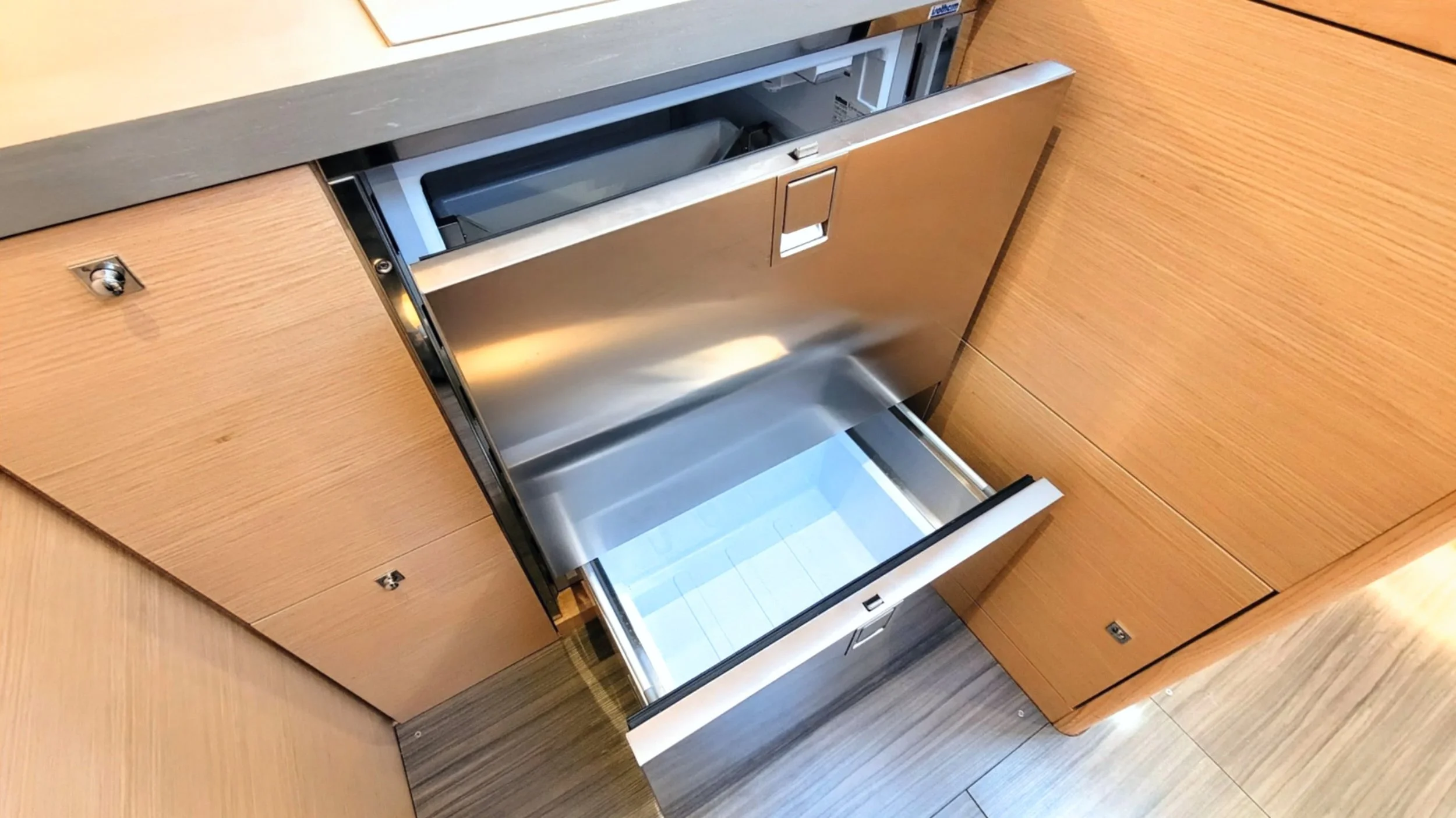 Open metal dishwasher with a wooden cabinet to the sides and floor.