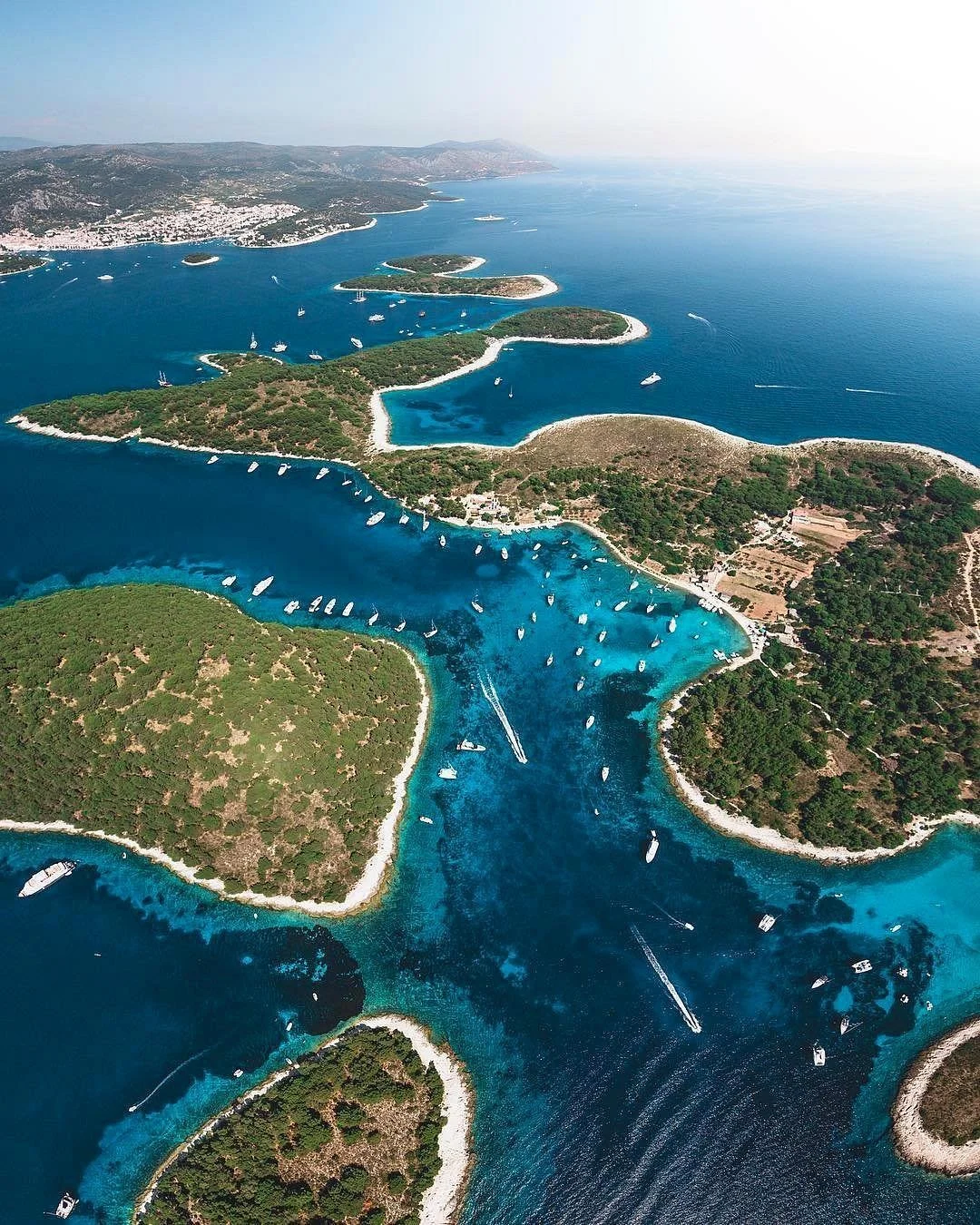Aerial view of turquoise waters, small islands with green vegetation, and boats in a coastal area