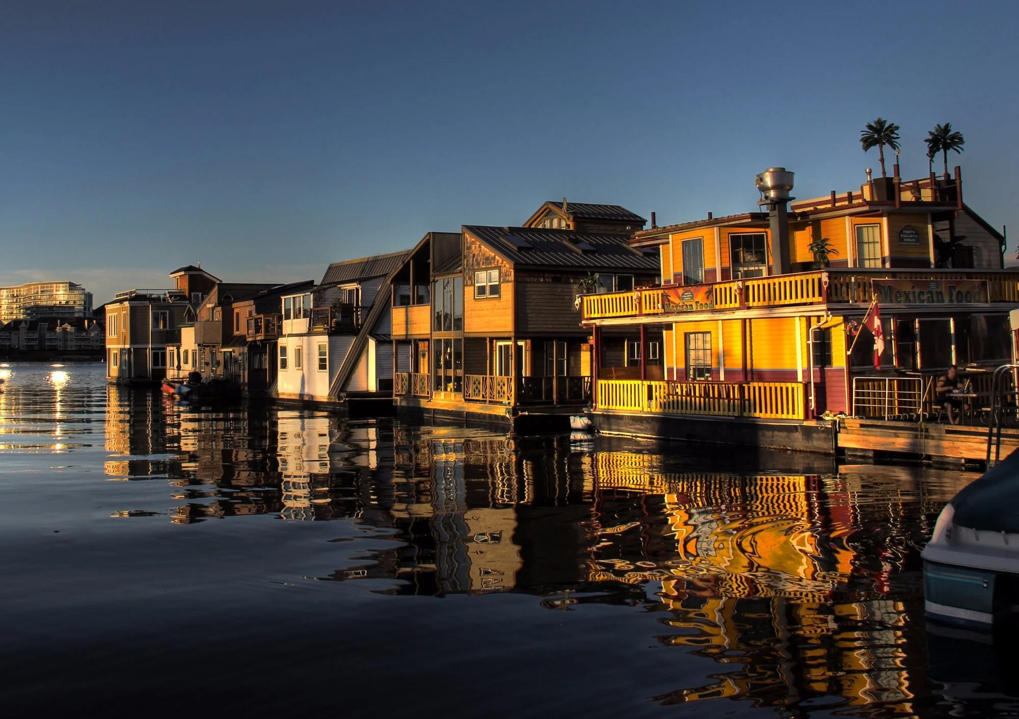 Colorful floating houses along a waterfront at sunset with reflections in the water.