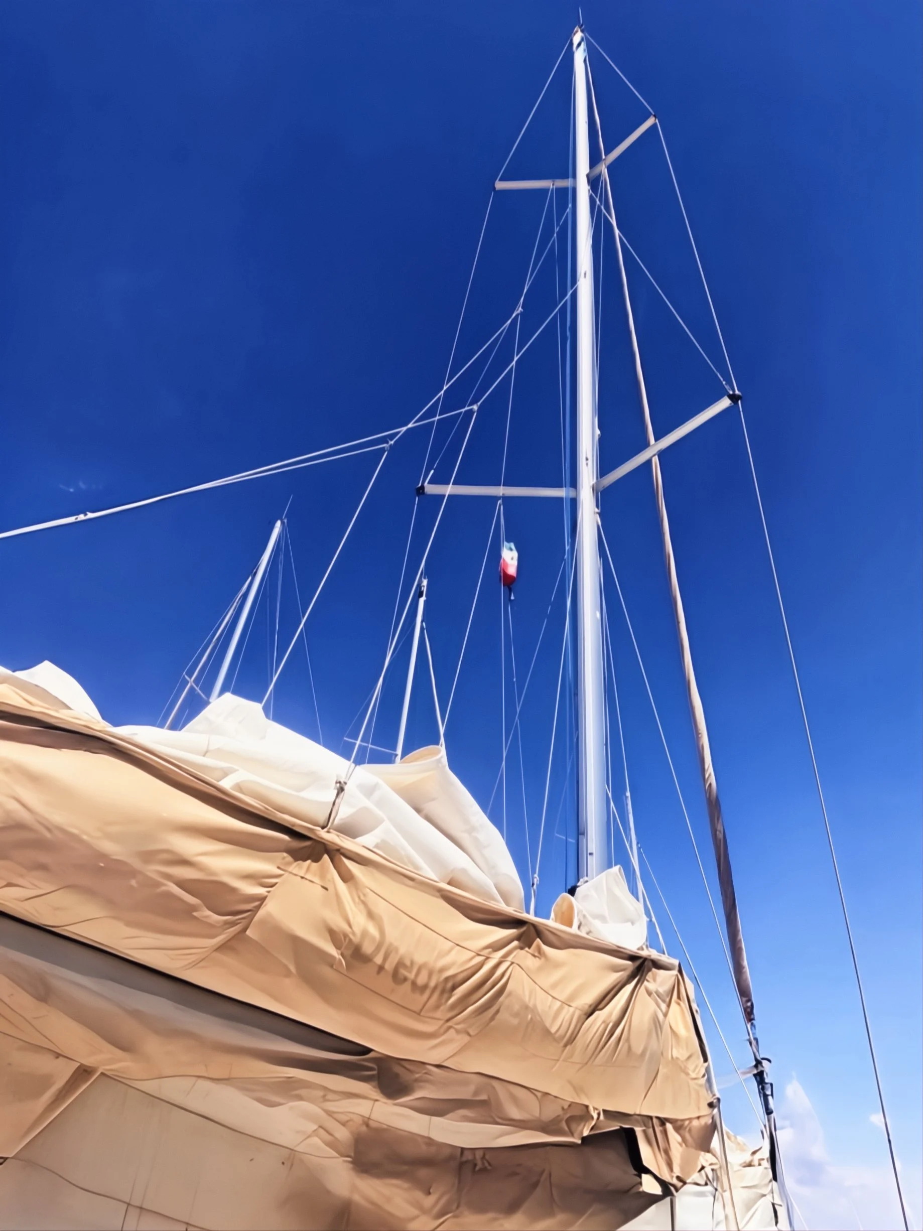 View of a sailboat with a tall mast and sails furled, against a clear blue sky.