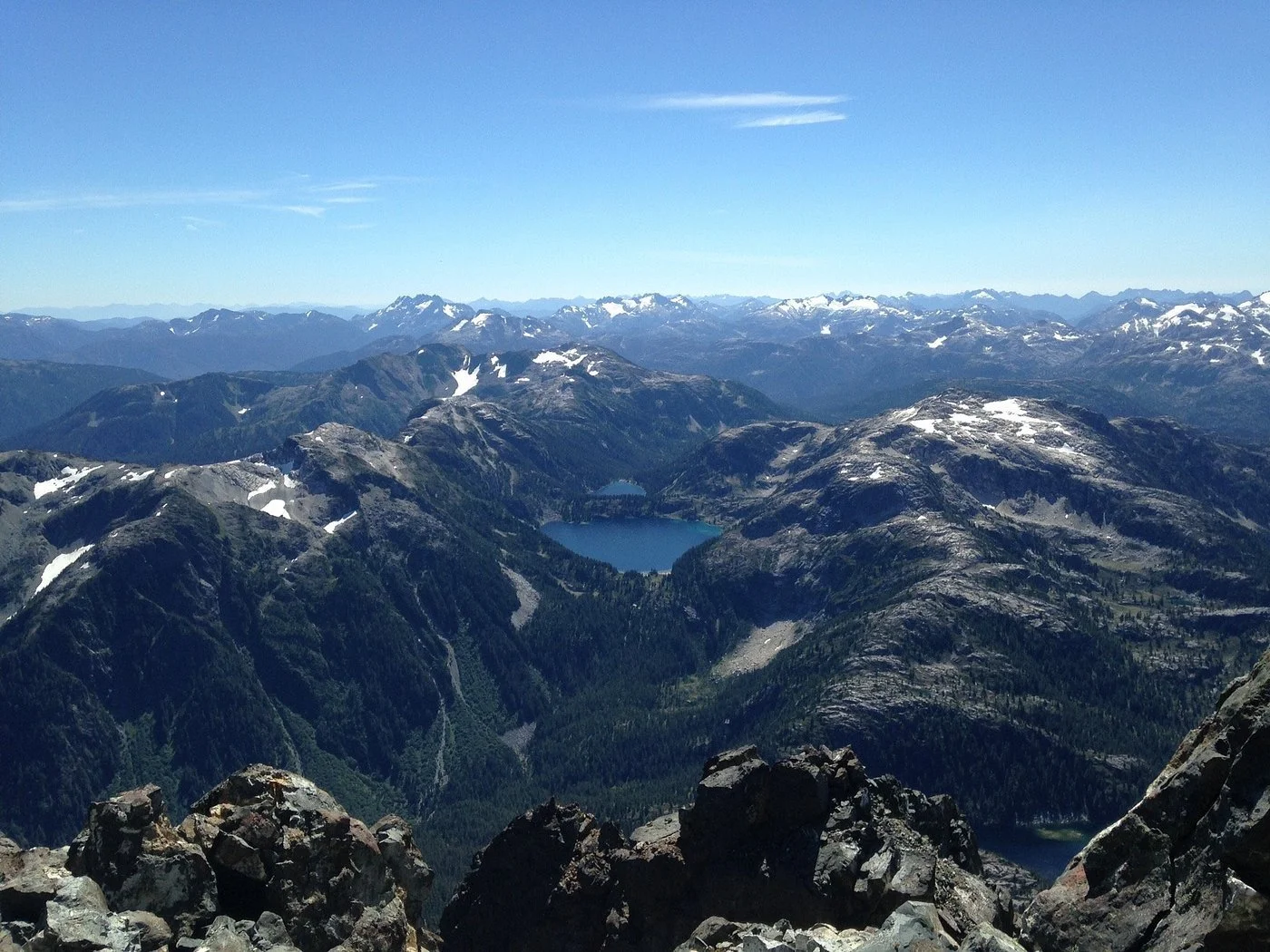 View of rugged mountains with snow patches, a lake at the base, and a clear blue sky above.