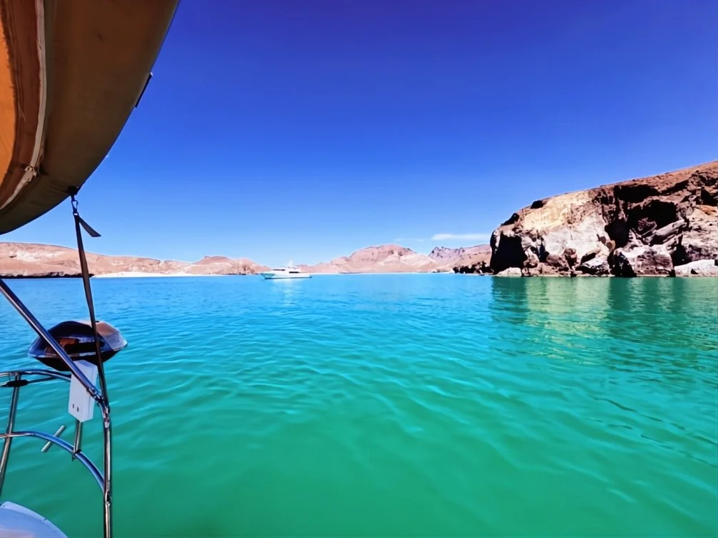 A view from a boat on a turquoise lake with rocky desert mountains in the background under a clear blue sky.