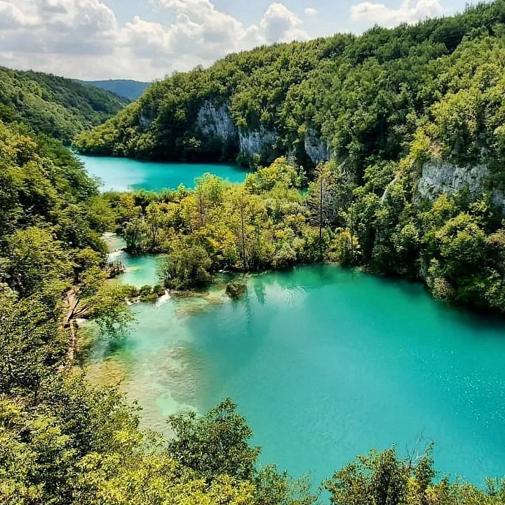 A scenic view of a winding river with clear turquoise water flowing through a lush green landscape with dense trees and white cliffs under a partly cloudy sky.