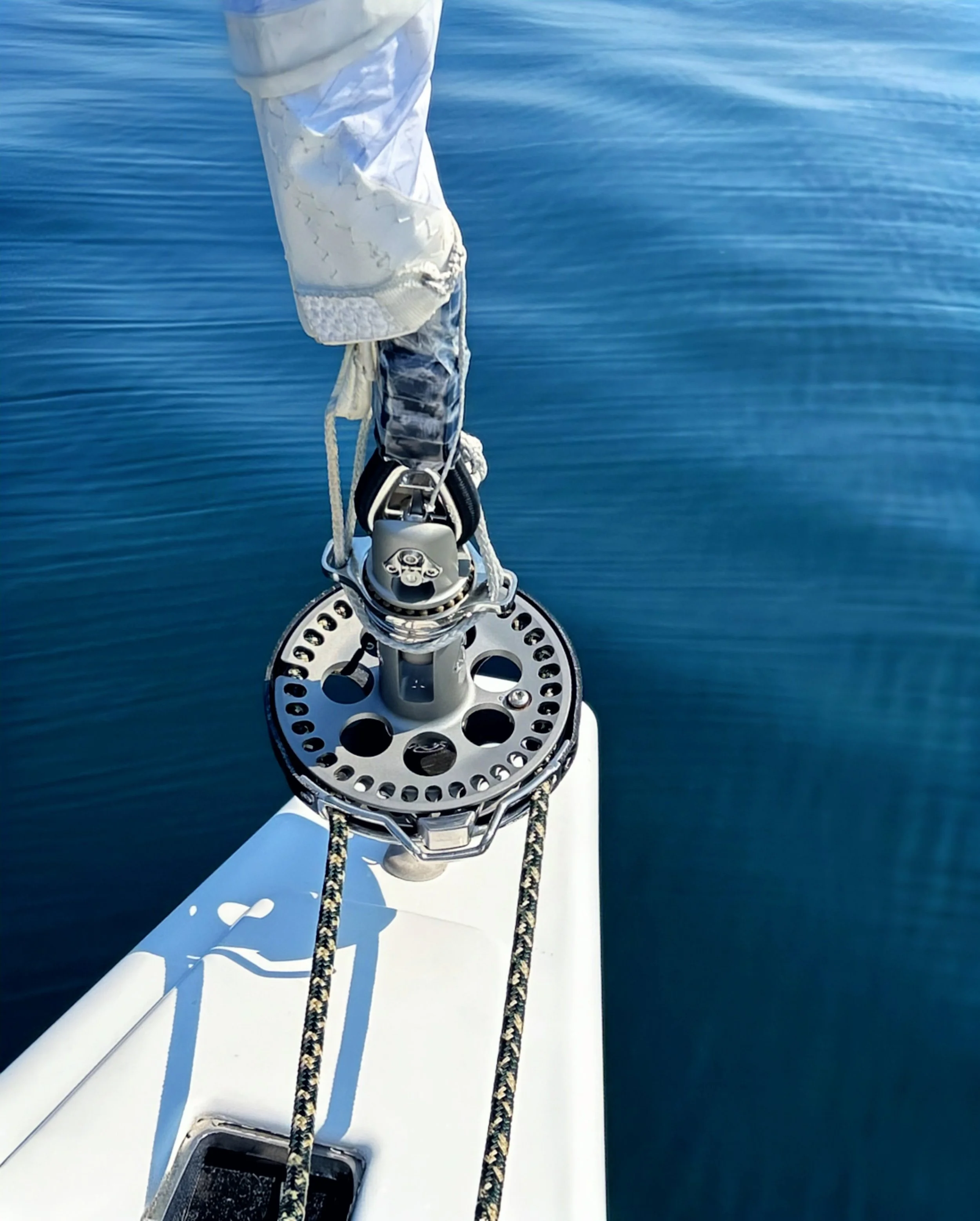 Close-up view of a boat's bow with its metal anchor windlass, ropes, and the water surrounding the boat.